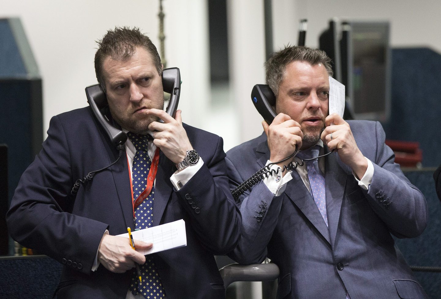 Two traders on the London Metals Exchange both holding two sets of telephone receivers, one held to each ear.