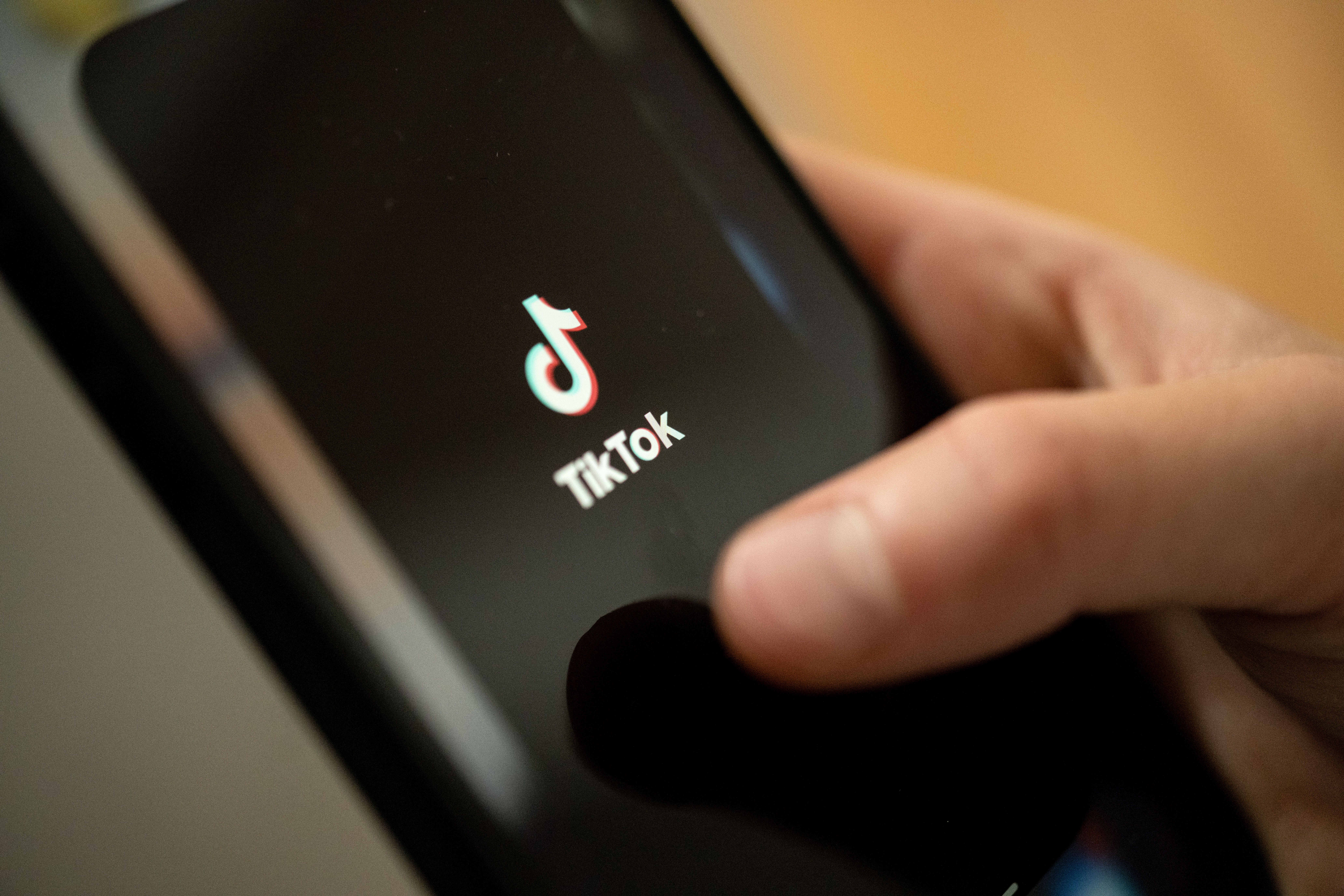 A person taps the TikTok logo on a smartphone.