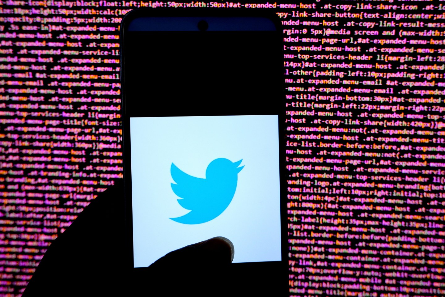 Twitter logo appearing on a phone screen in front of lines of code in the background