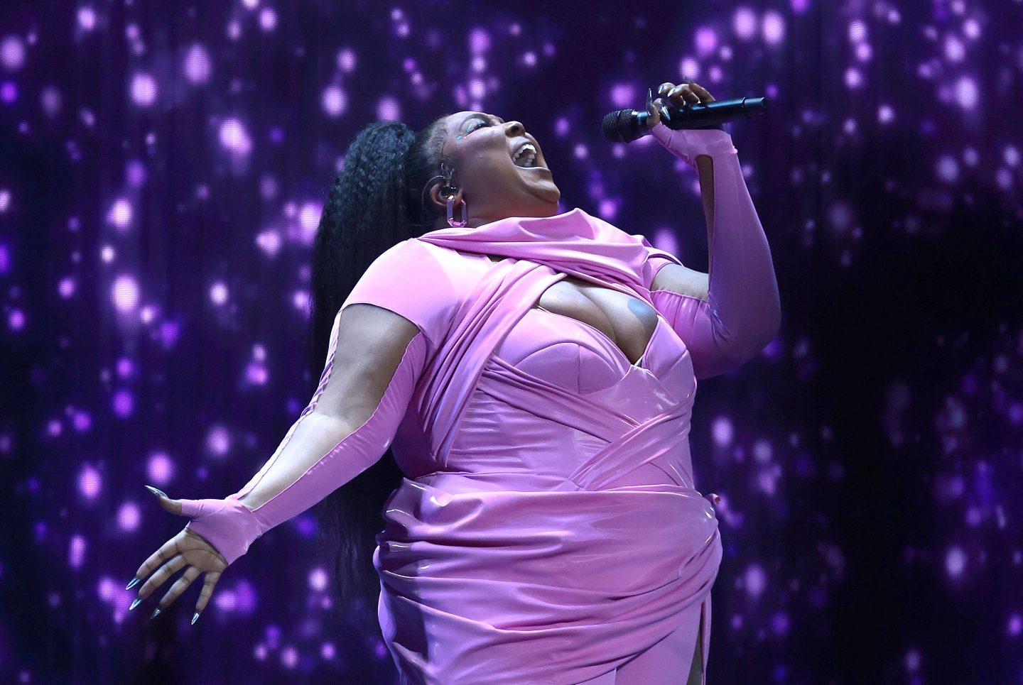 Lizzo holding a mic while singing on a stage.