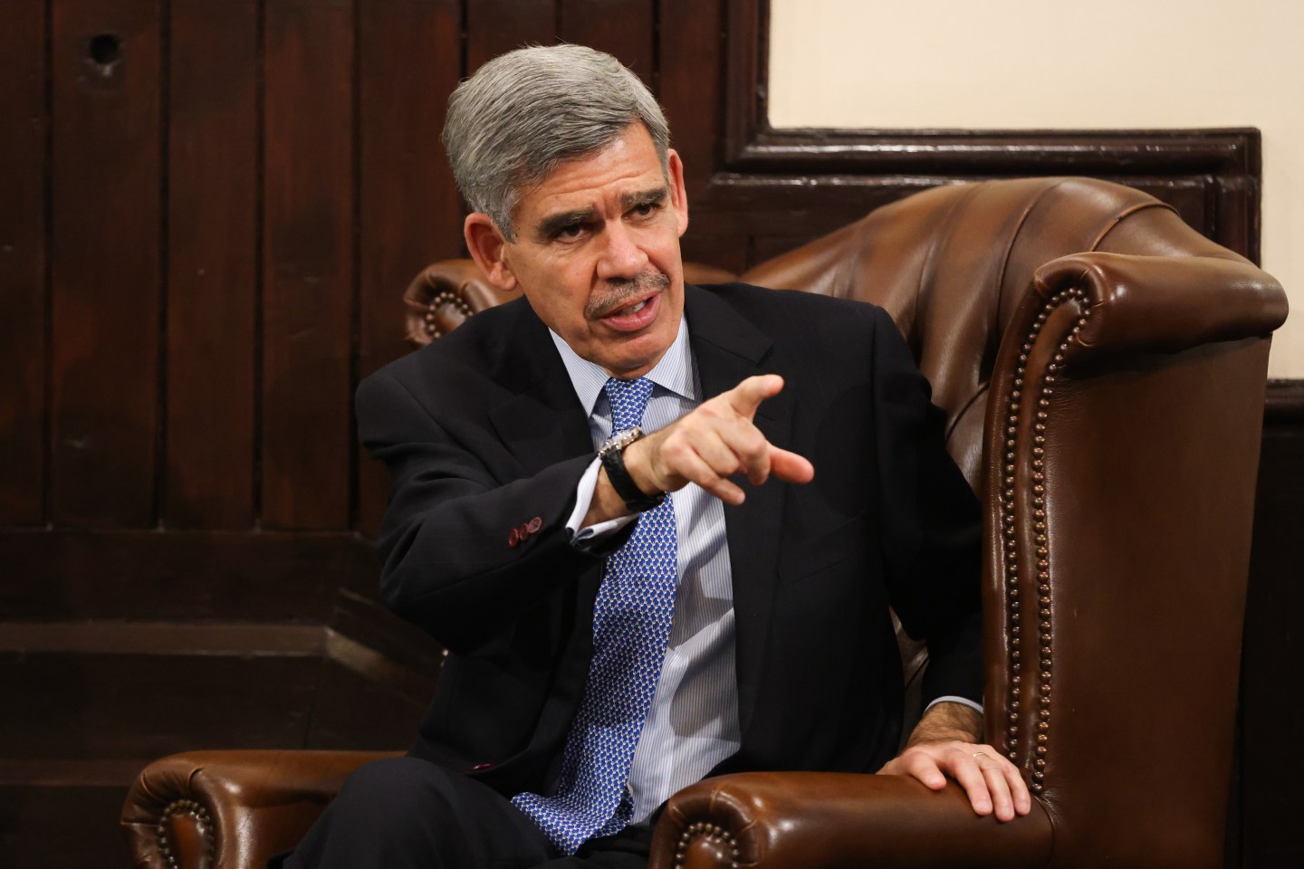 Portrait of Mohamed El-Erian sitting in an armchair pointing towards a camera