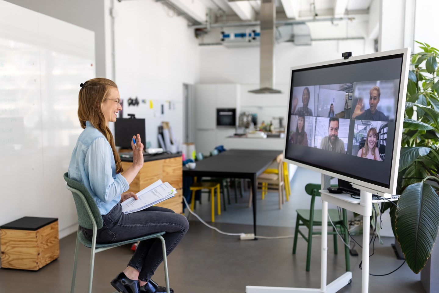 Female professional having online meeting with team seen on big television screen. Businesswoman in hybrid office space having web conference with coworkers.