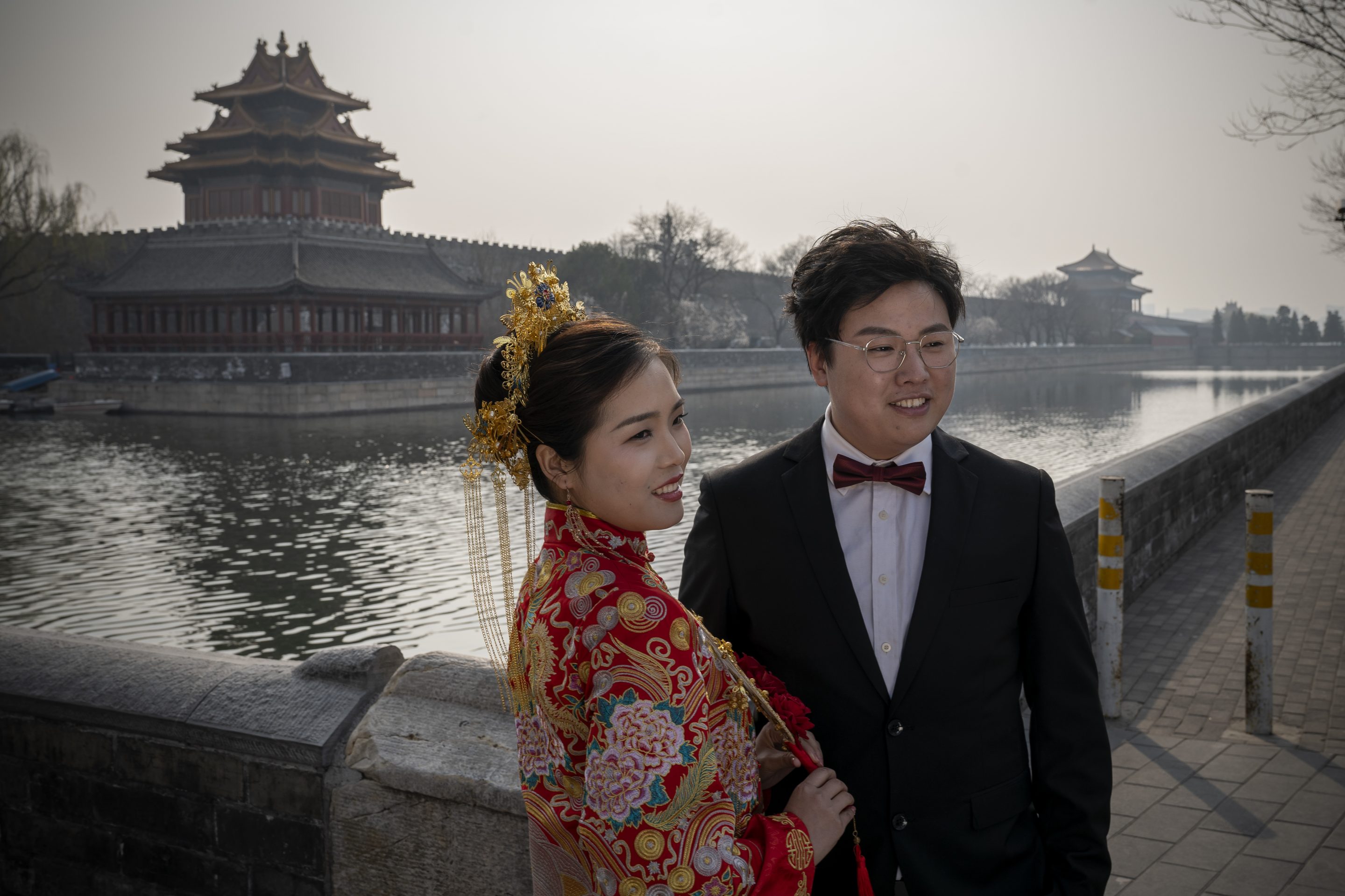 A bride and groom dressed in traditional wedding costumes pose in front of the Forbidden City in Beijing, China, on March 23, 2022.