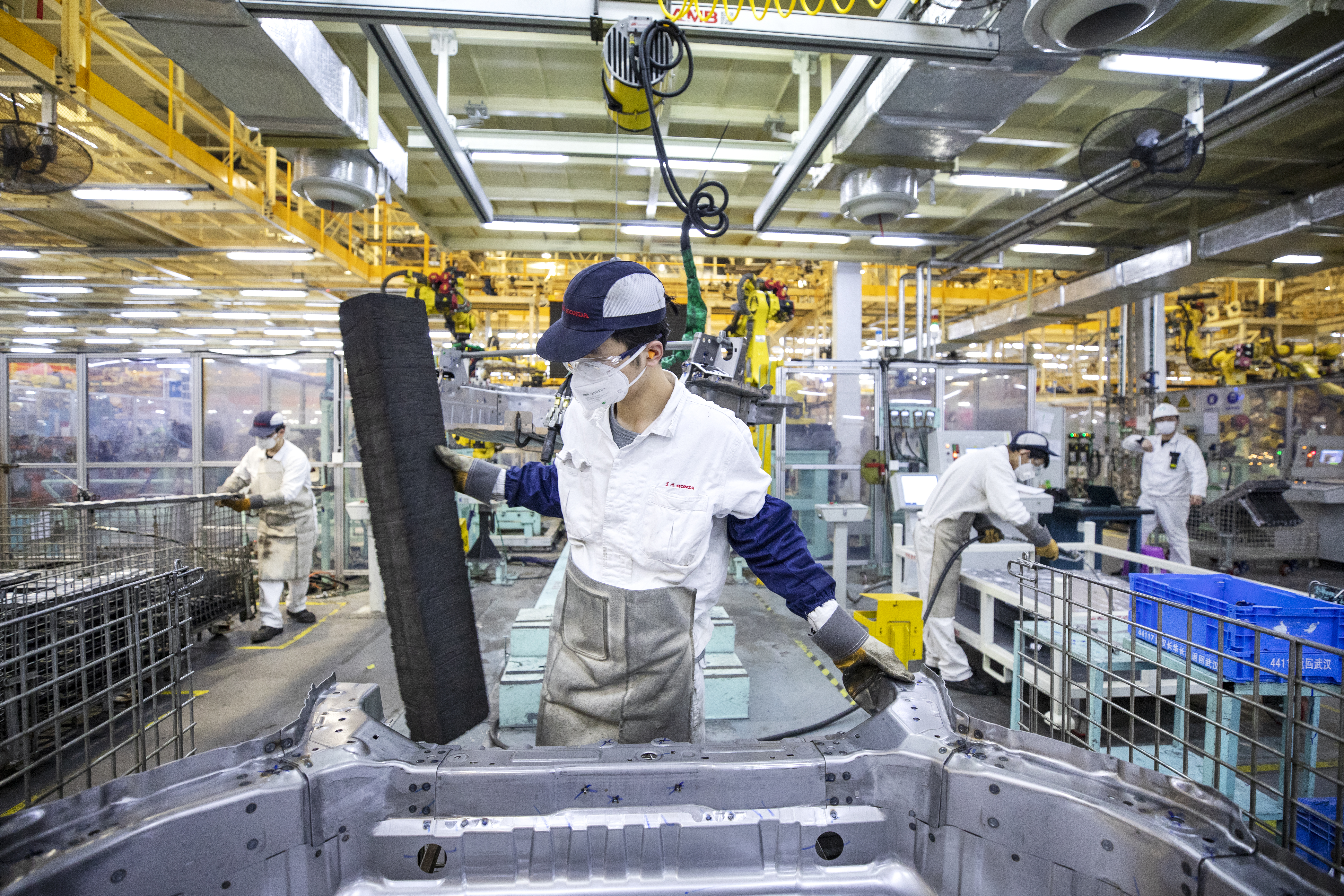 Shot of a worker assembling a car on a Honda assembly line with more workers in the background
