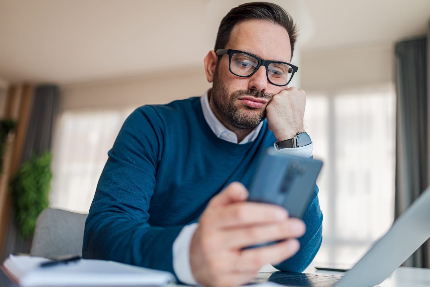 A man in a blue sweater looks at his smartphone while working