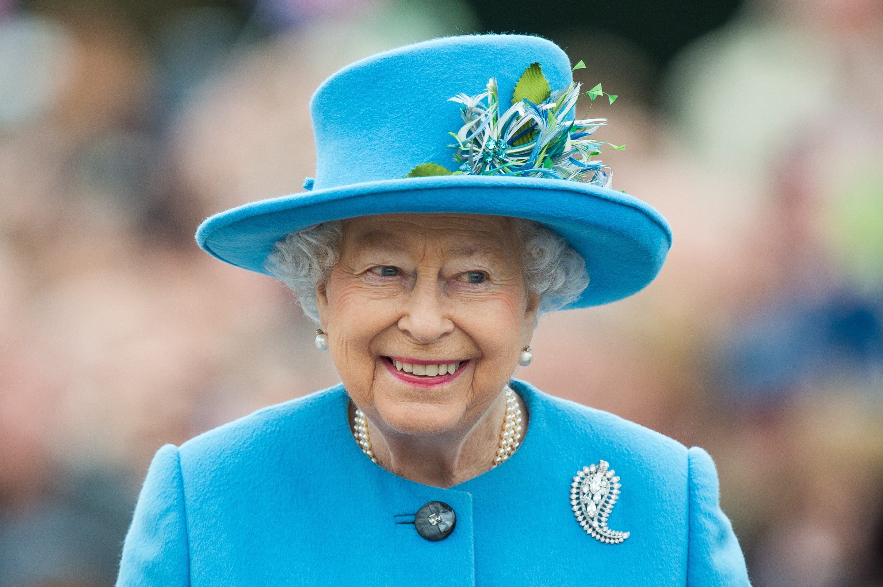 An elderly woman with white hair, wearing a blue-brimmed hat, smiles