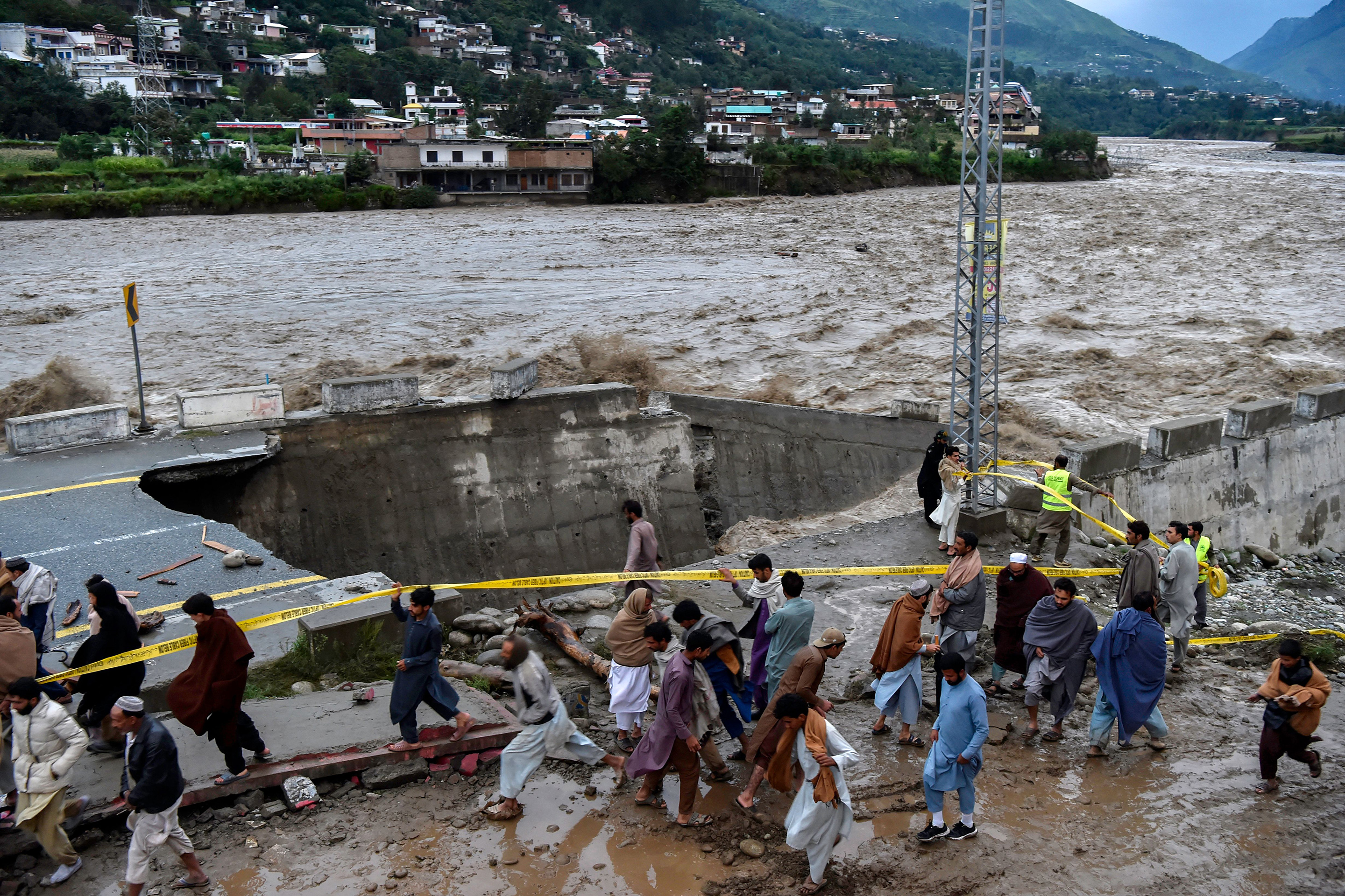 People gather in front of a road damaged by flood waters following heavy monsoon rains in in Pakistan's northern Swat Valley.