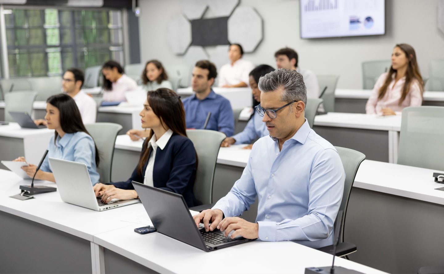 Group of MBA students sit using their laptops in a classroom.