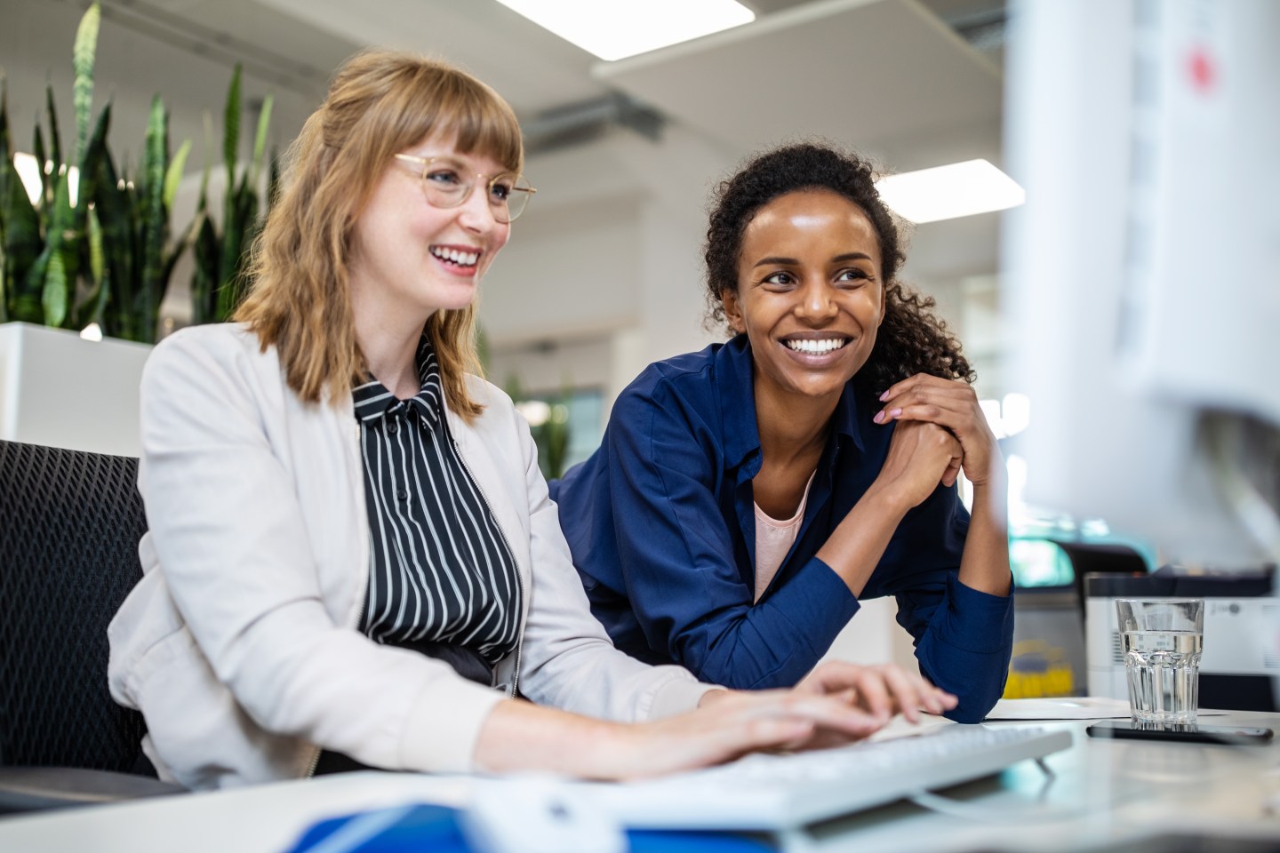 Multi-ethnic female entrepreneurs smiling while looking at computer in creative office