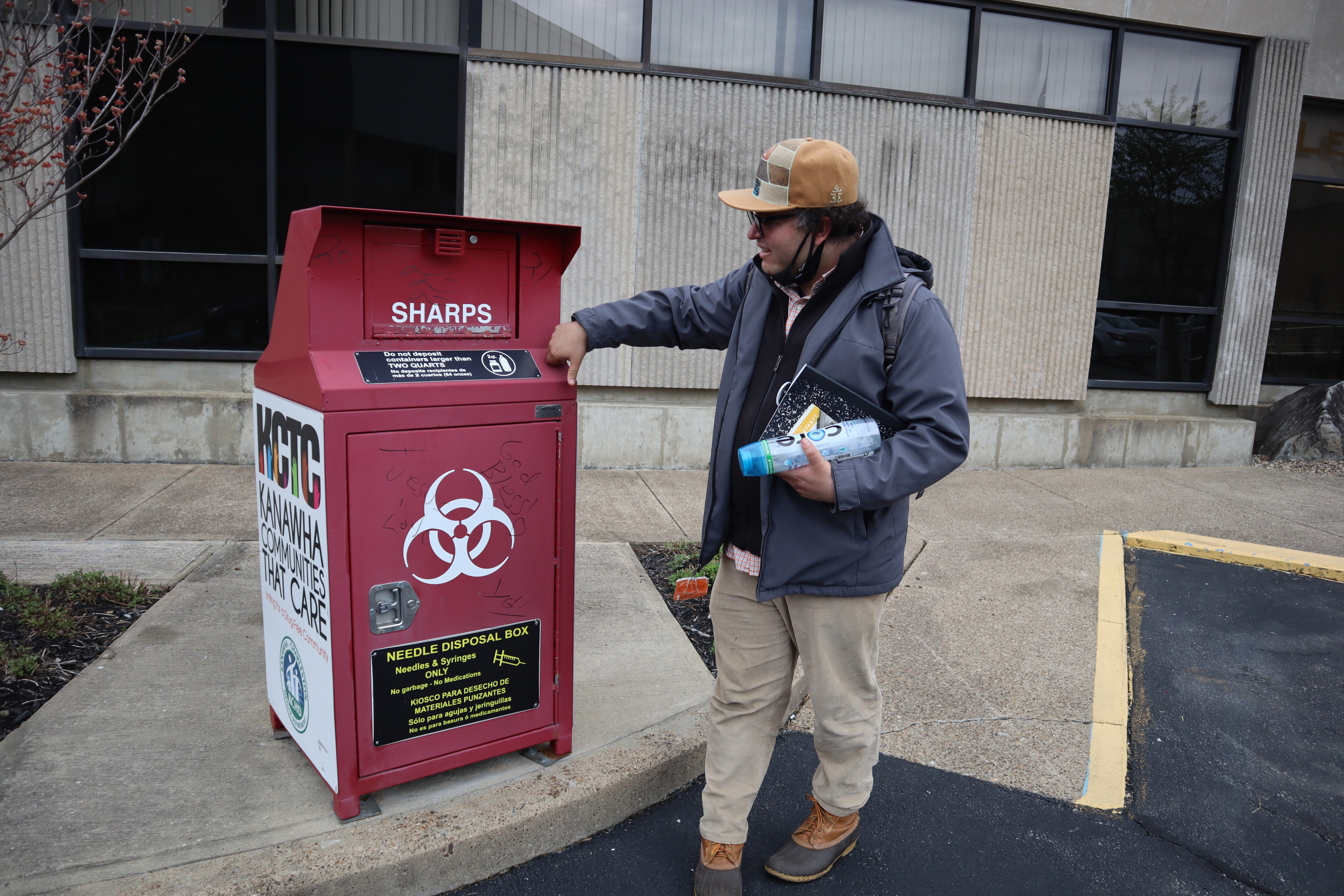 A man stands in front of a syringe disposal box.