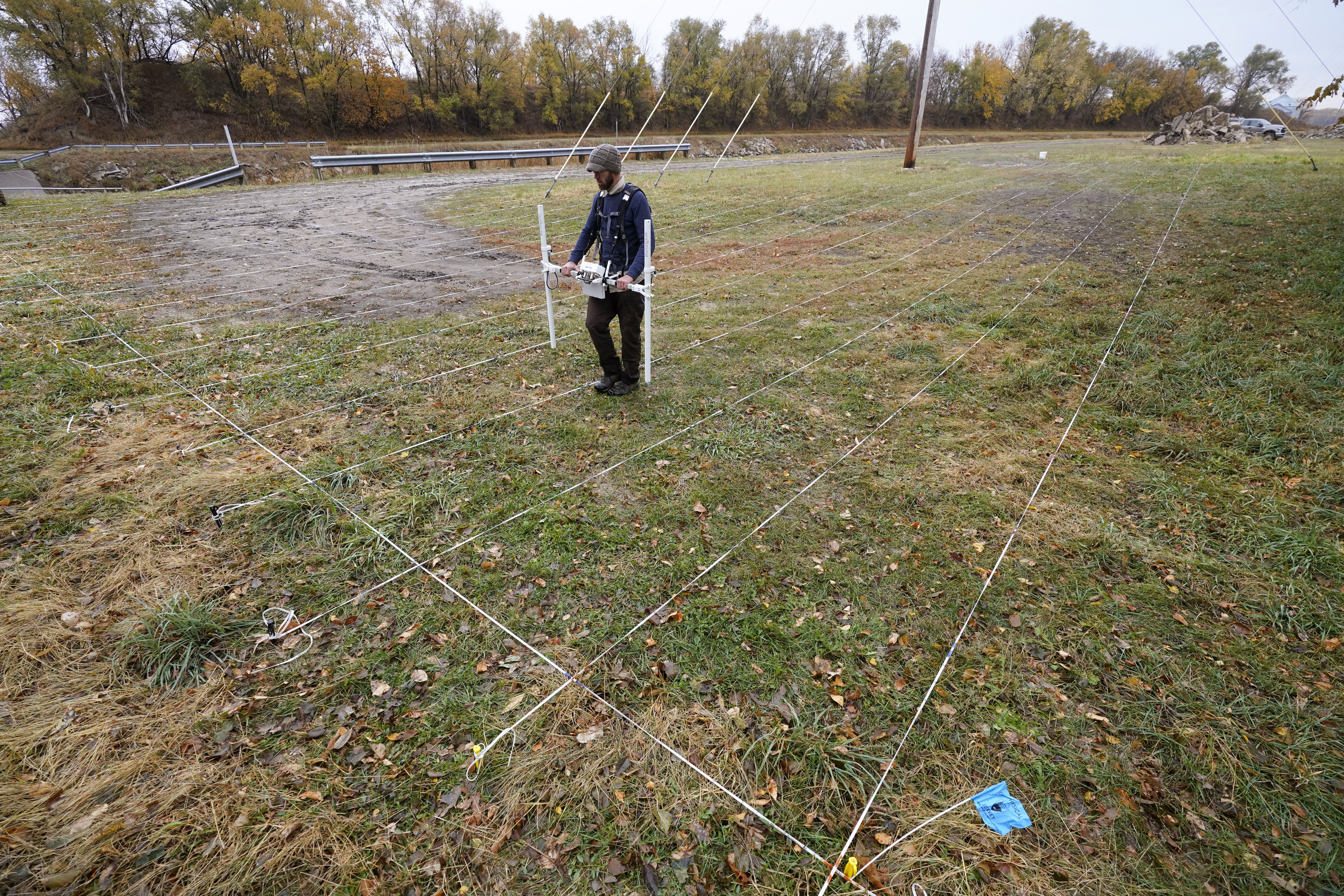 A man walks across a lawn using radar to find graves.