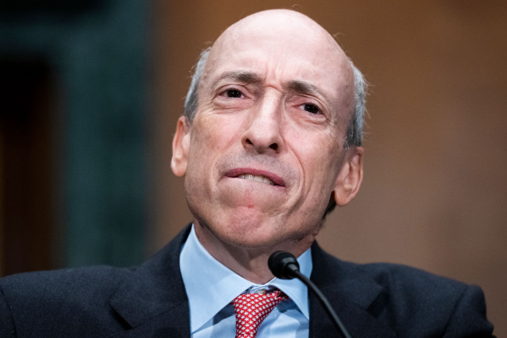 A white man with a blue shirt and orange tie speaks into a microphone