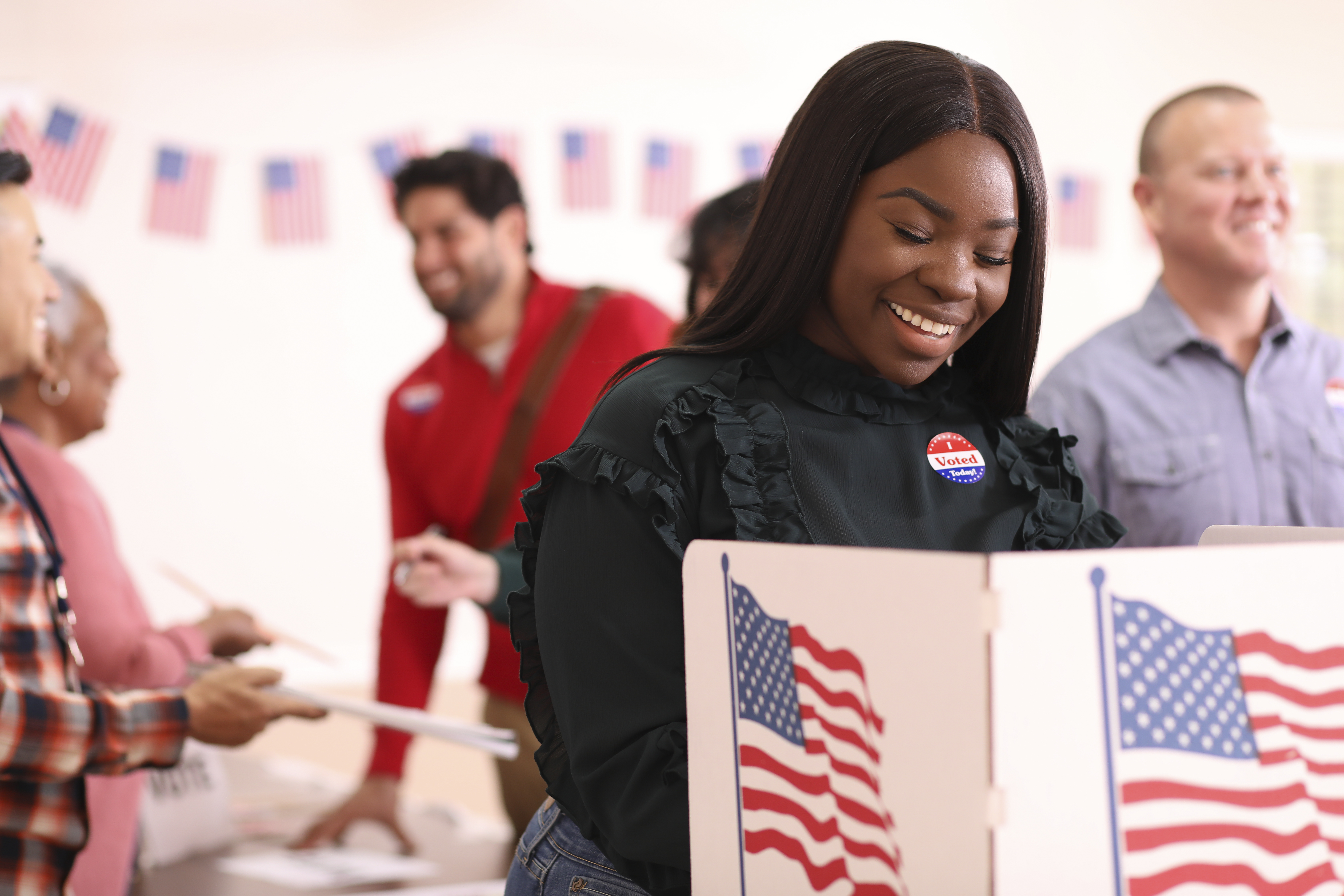 A Black women stands in front of a voting booth.