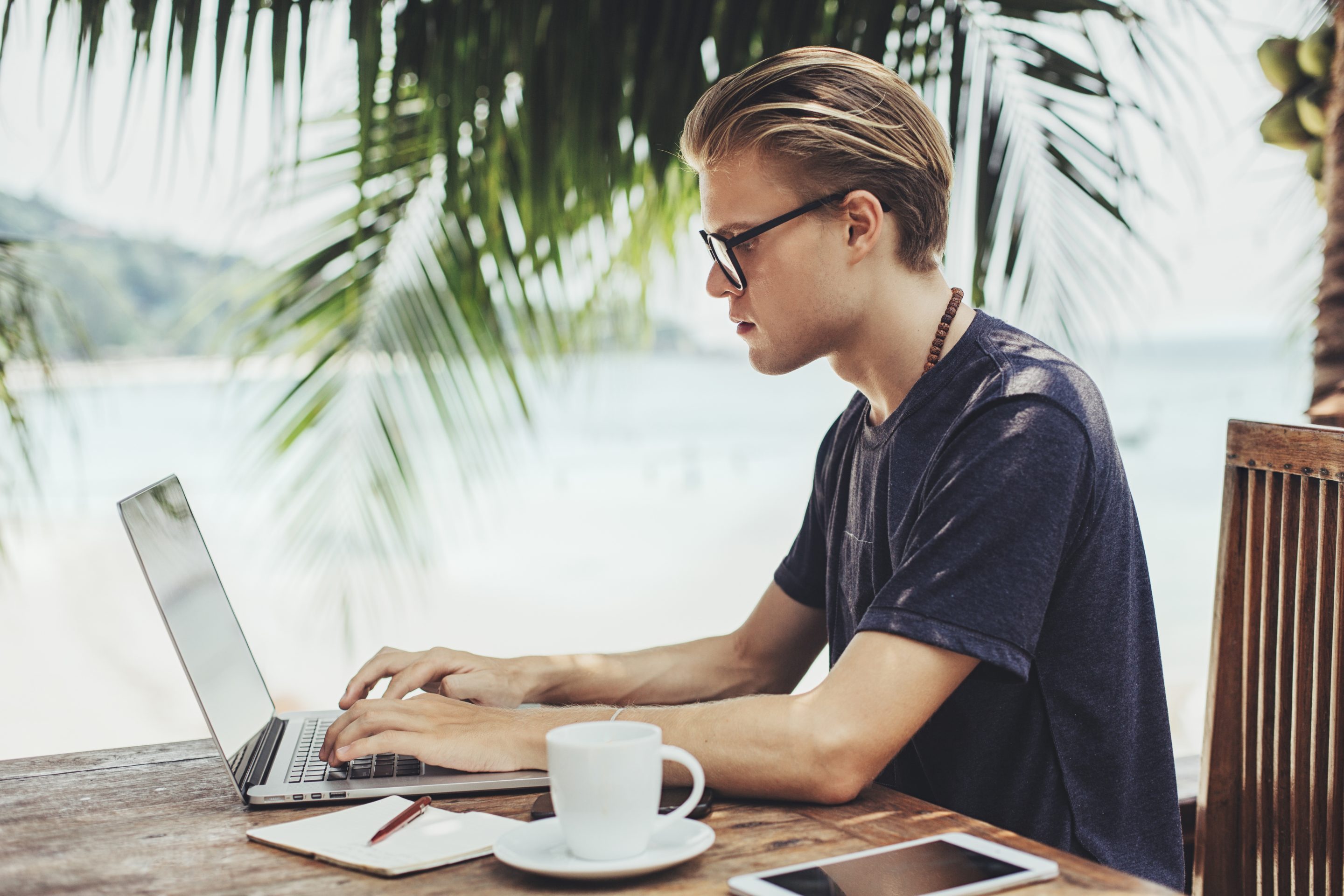 A worker by a tropical beach on laptop