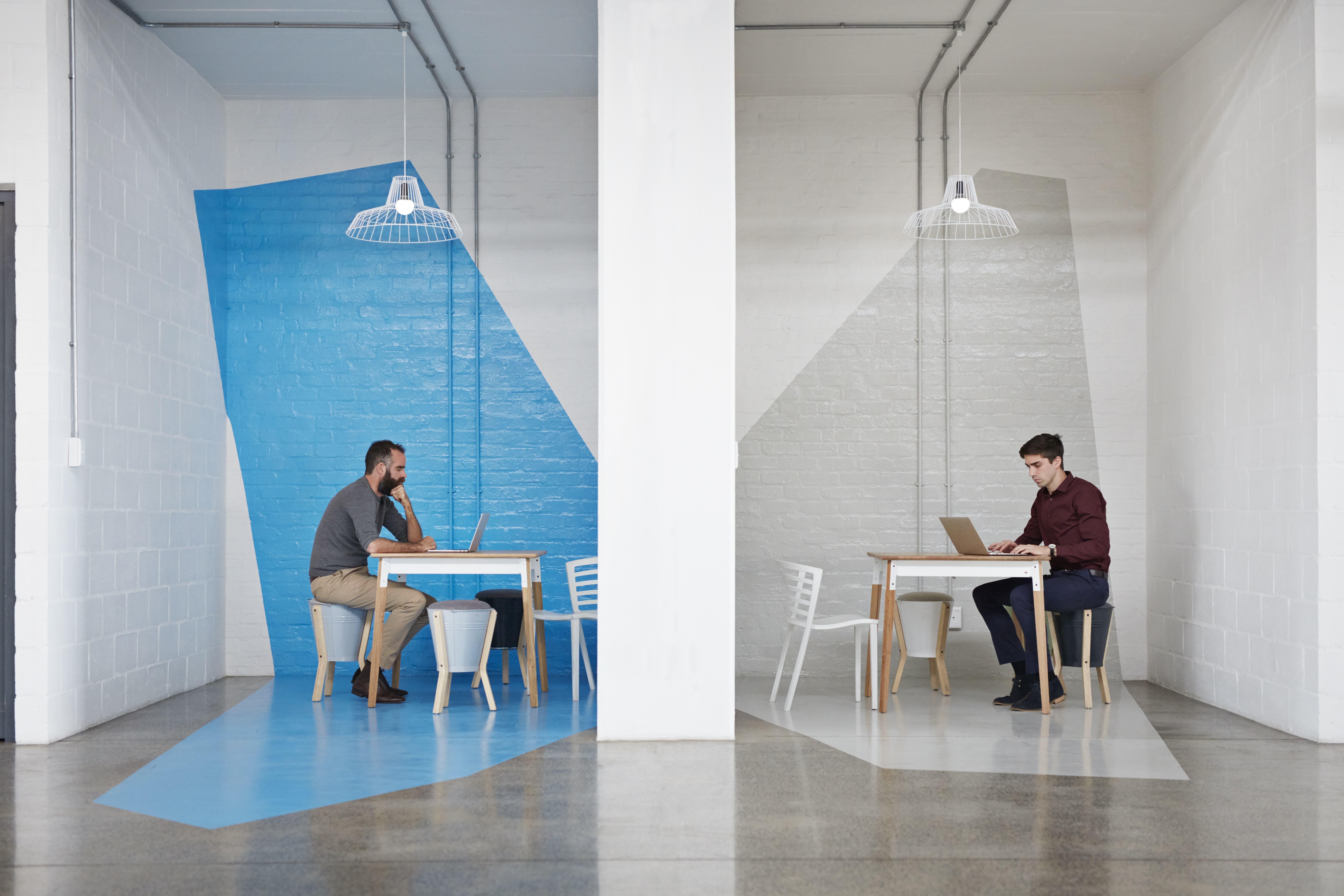 Two people sit on opposite sides of a wall working on their laptops