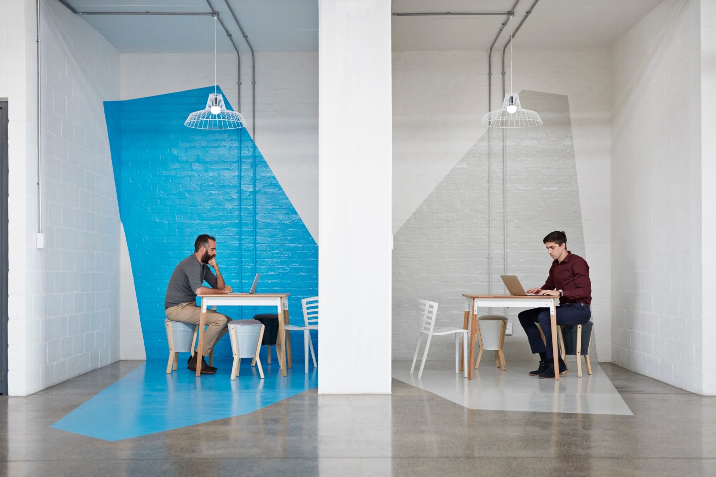 Two people sit on opposite sides of a wall working on their laptops