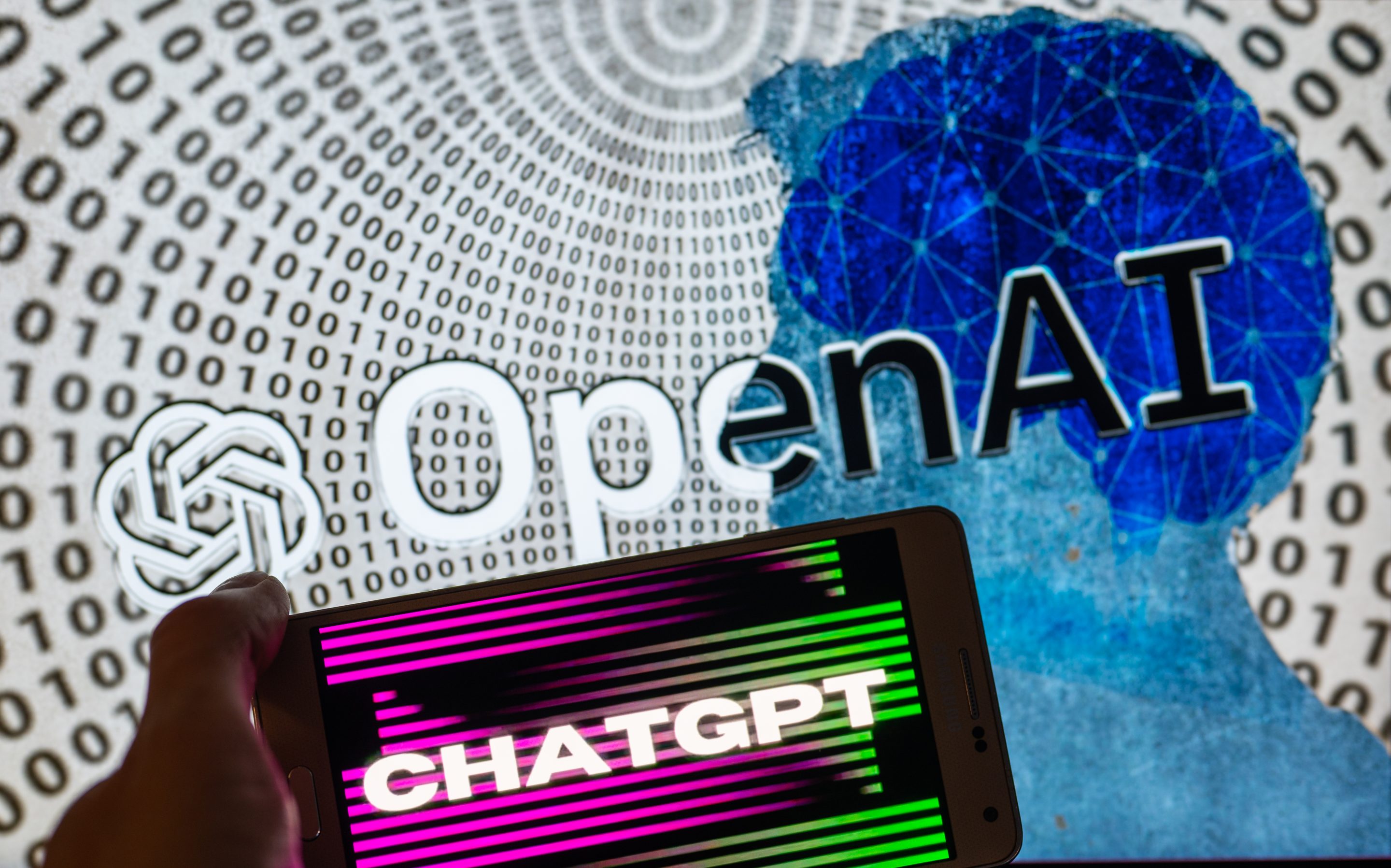 OpenAI logo seen on screen with ChatGPT website displayed on mobile