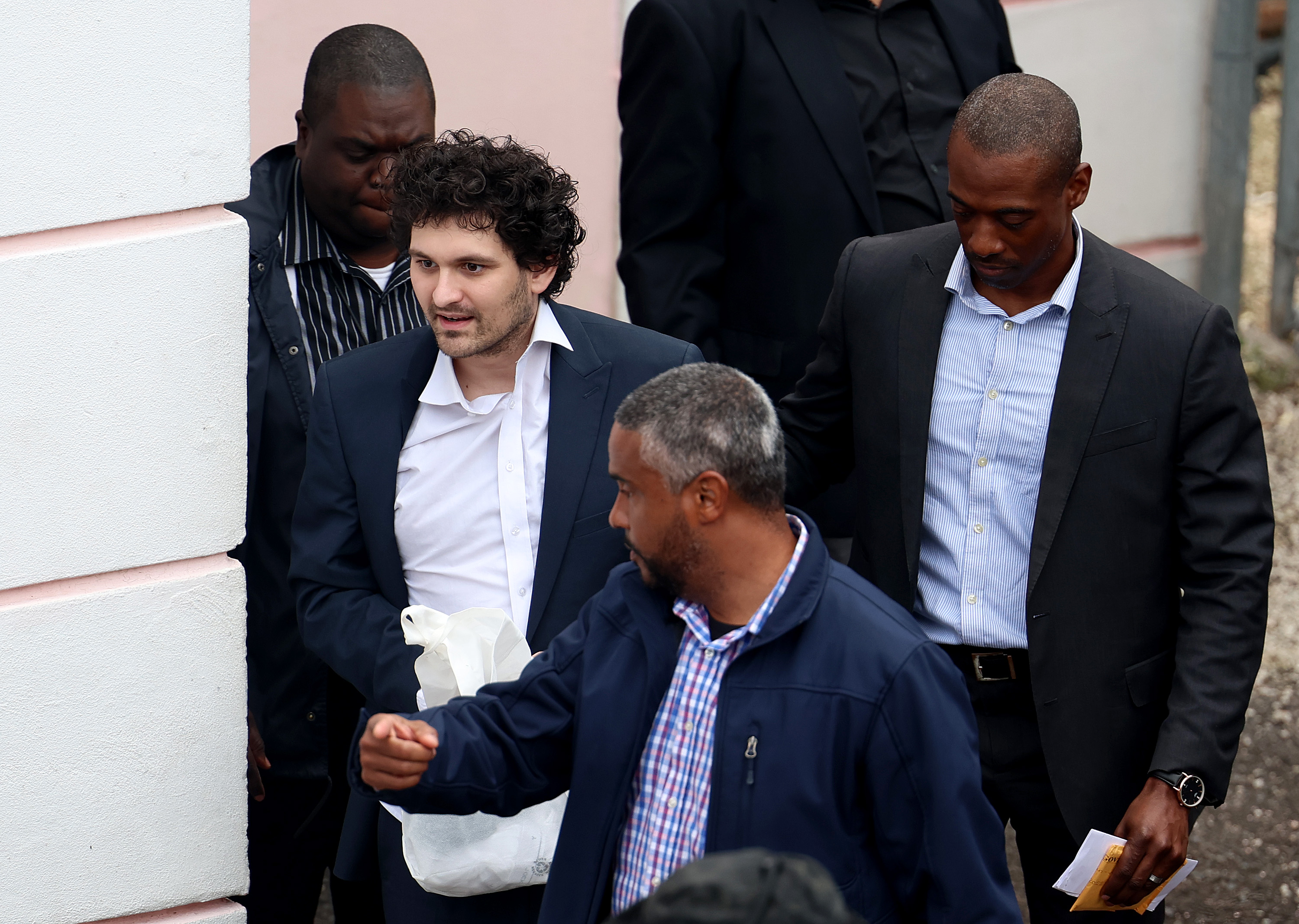 Sam Bankman-Fried surrounded by authorities in the Bahamas.