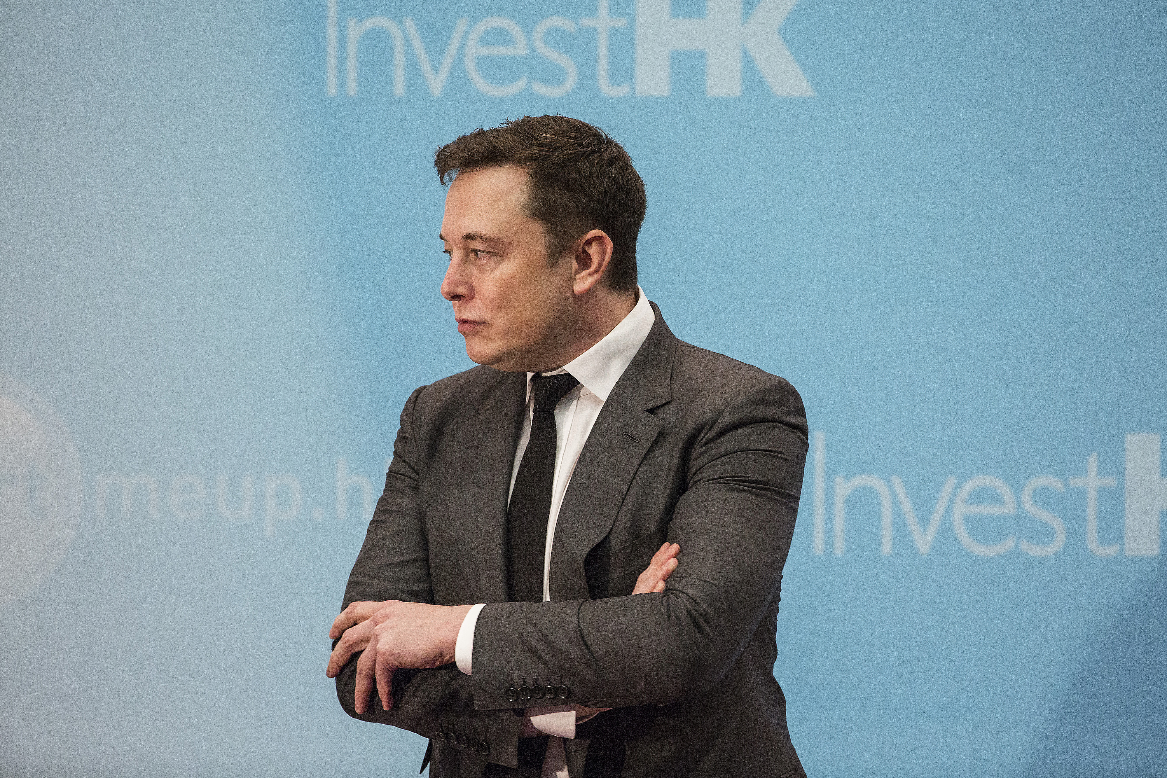 Elon Musk standing on stage with arms crossed