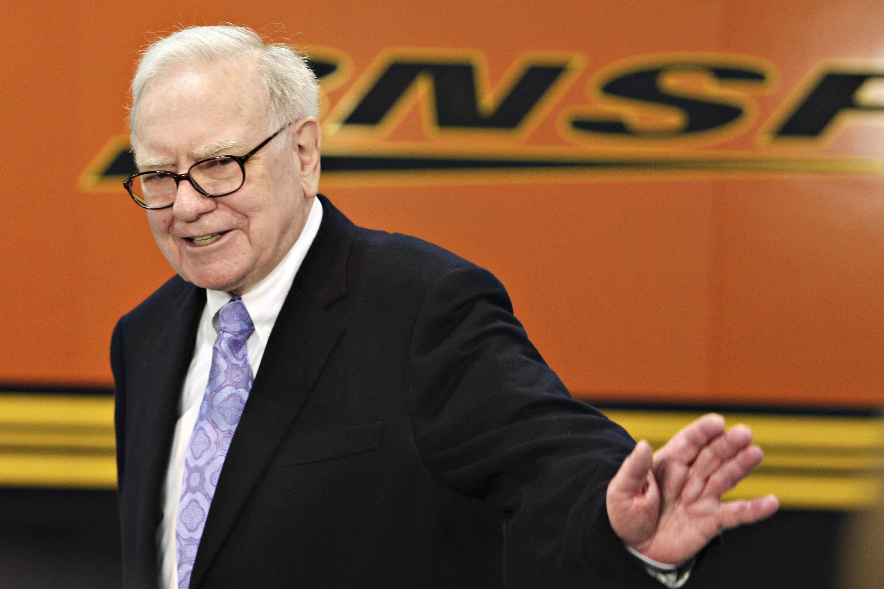 Warren Buffett standing in front of a BNSF railroad logo.