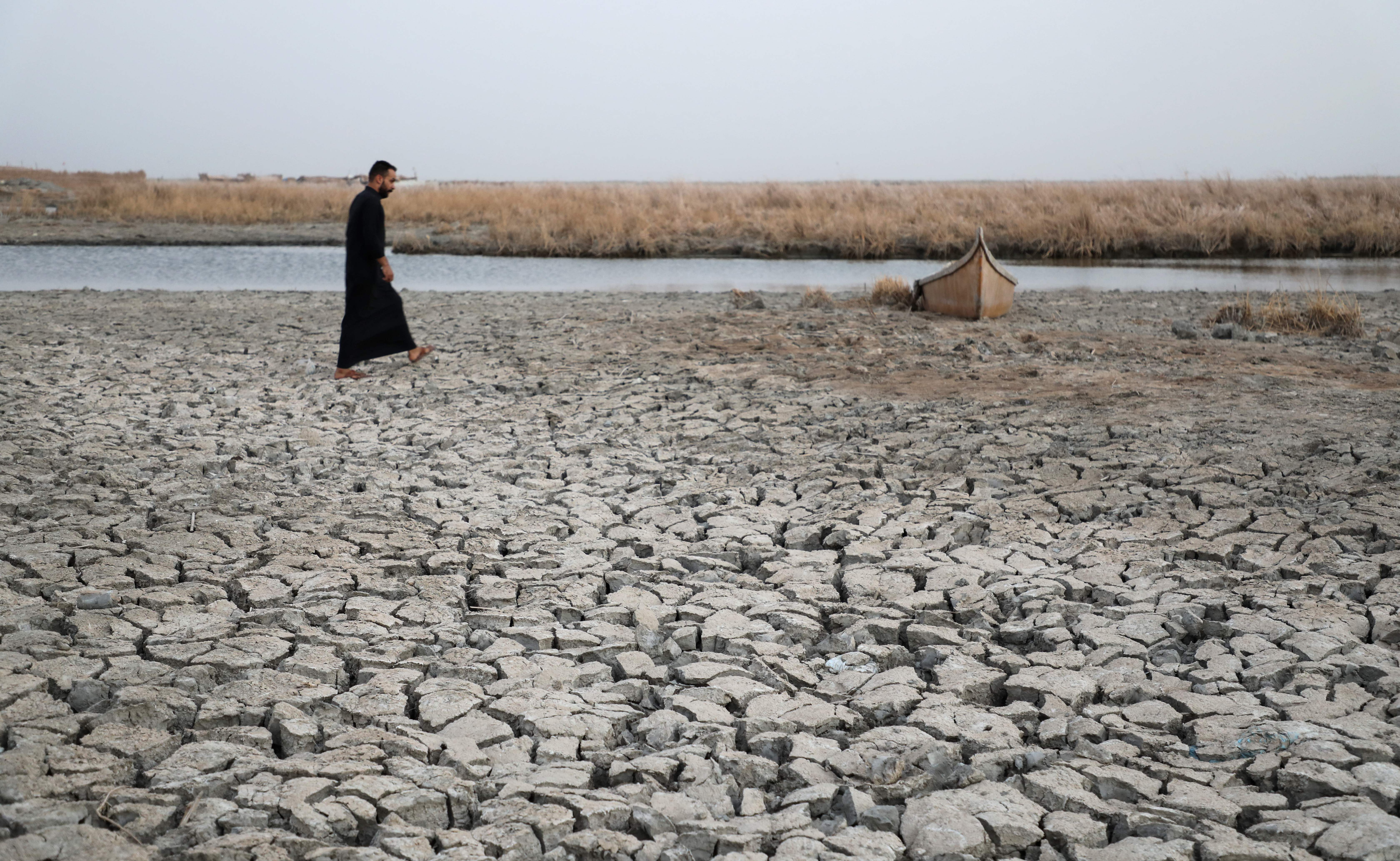 A man walks past a stuck boat in a dried-out riverbed in Iraq