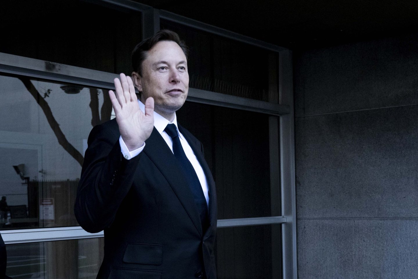 Elon Musk waving to a crowd outside a courthouse