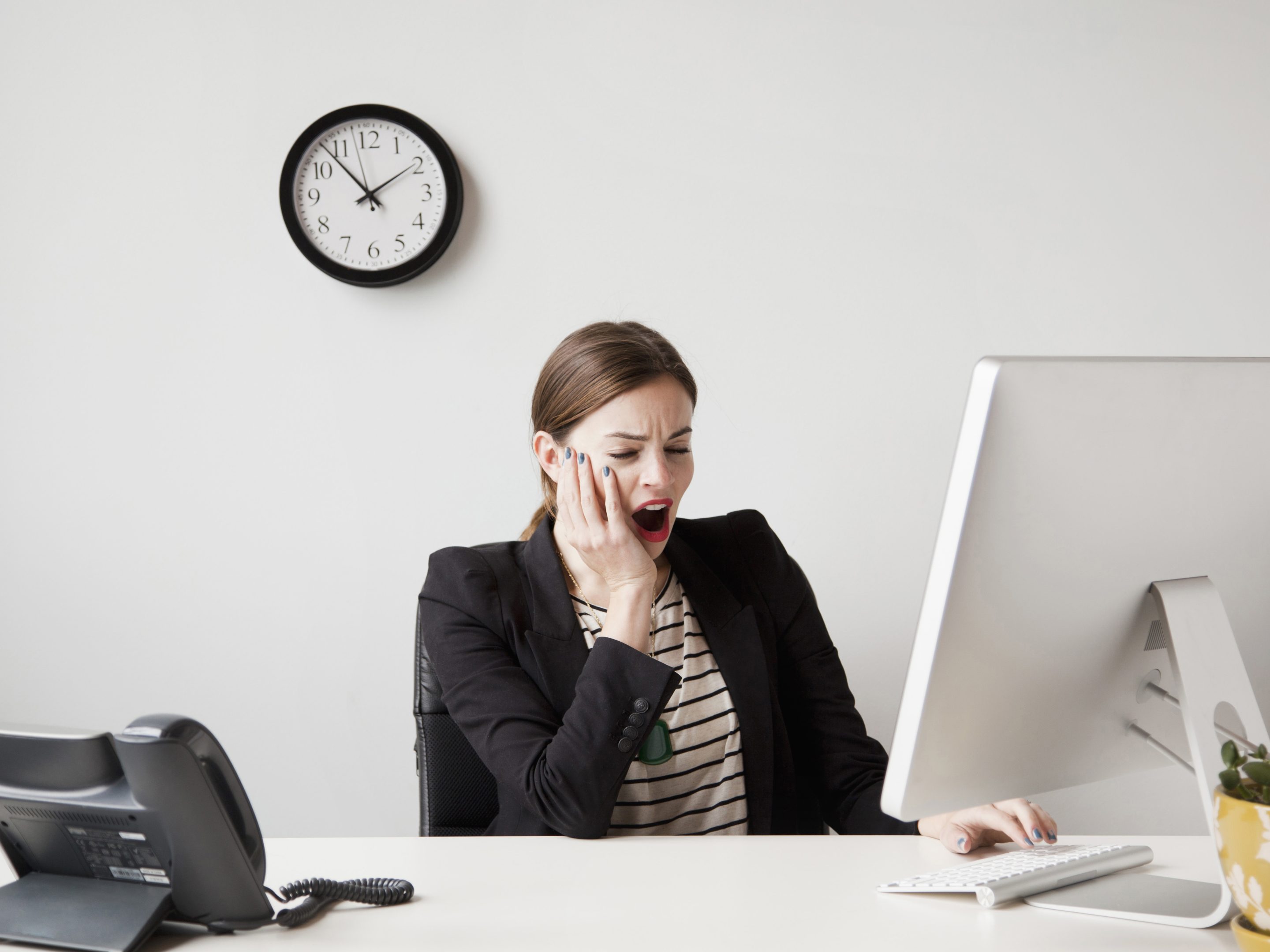 Young businesswoman yawning and looking bored in front of her computer in an office