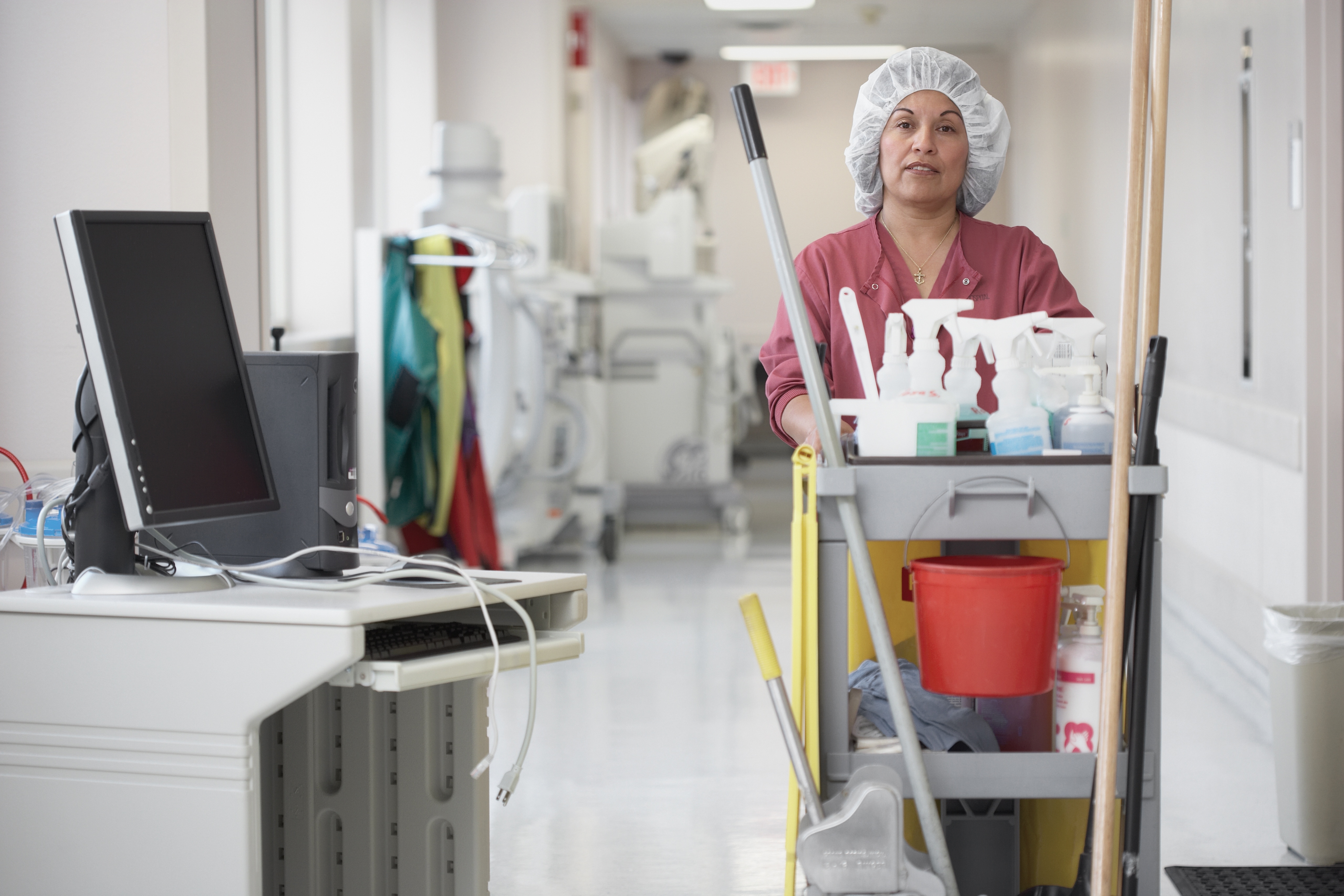 A cleaning woman pushing a cart through a hospital corridor