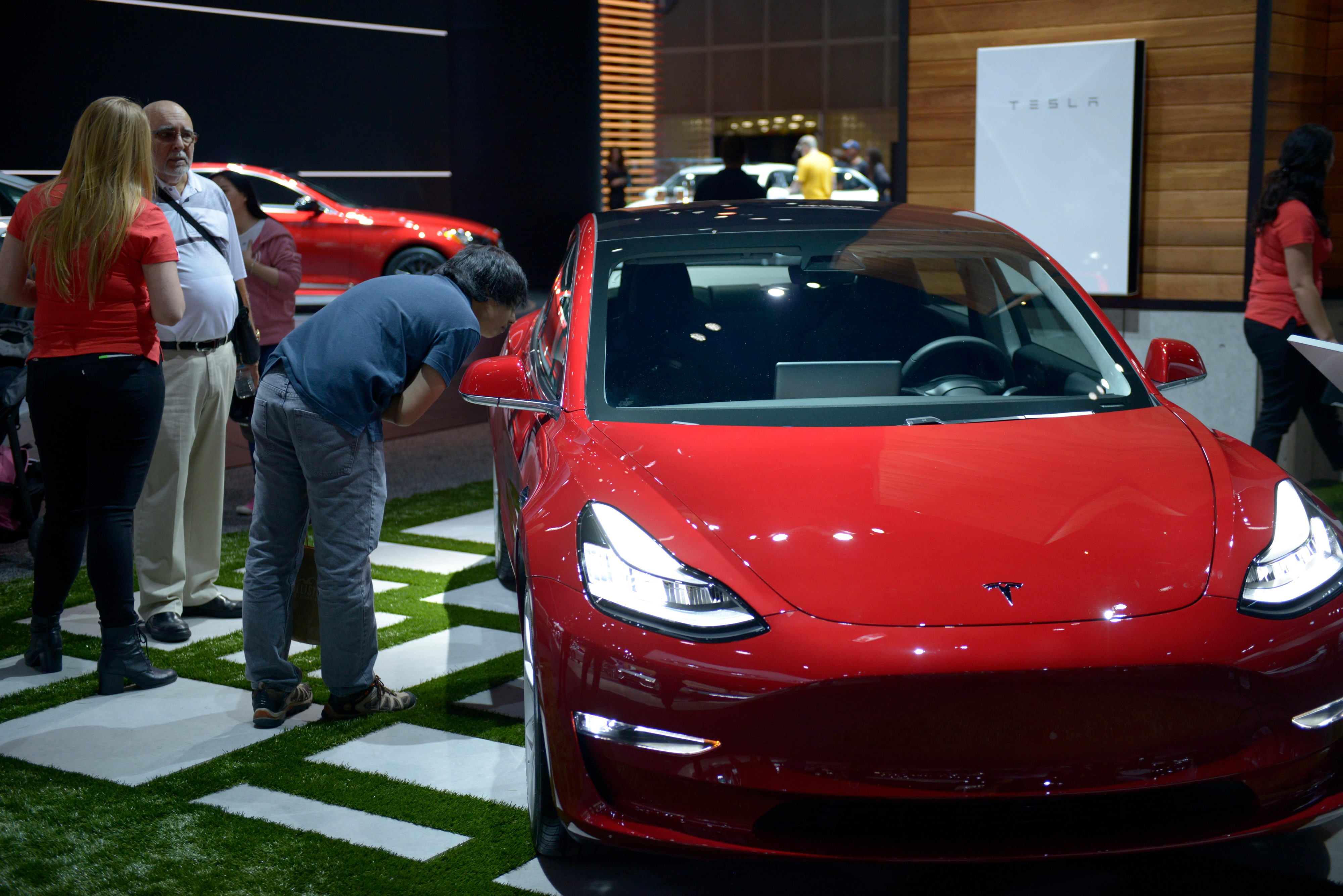 People inspect the Tesla Model 3 as it sits on display at the Los Angeles Auto Show.