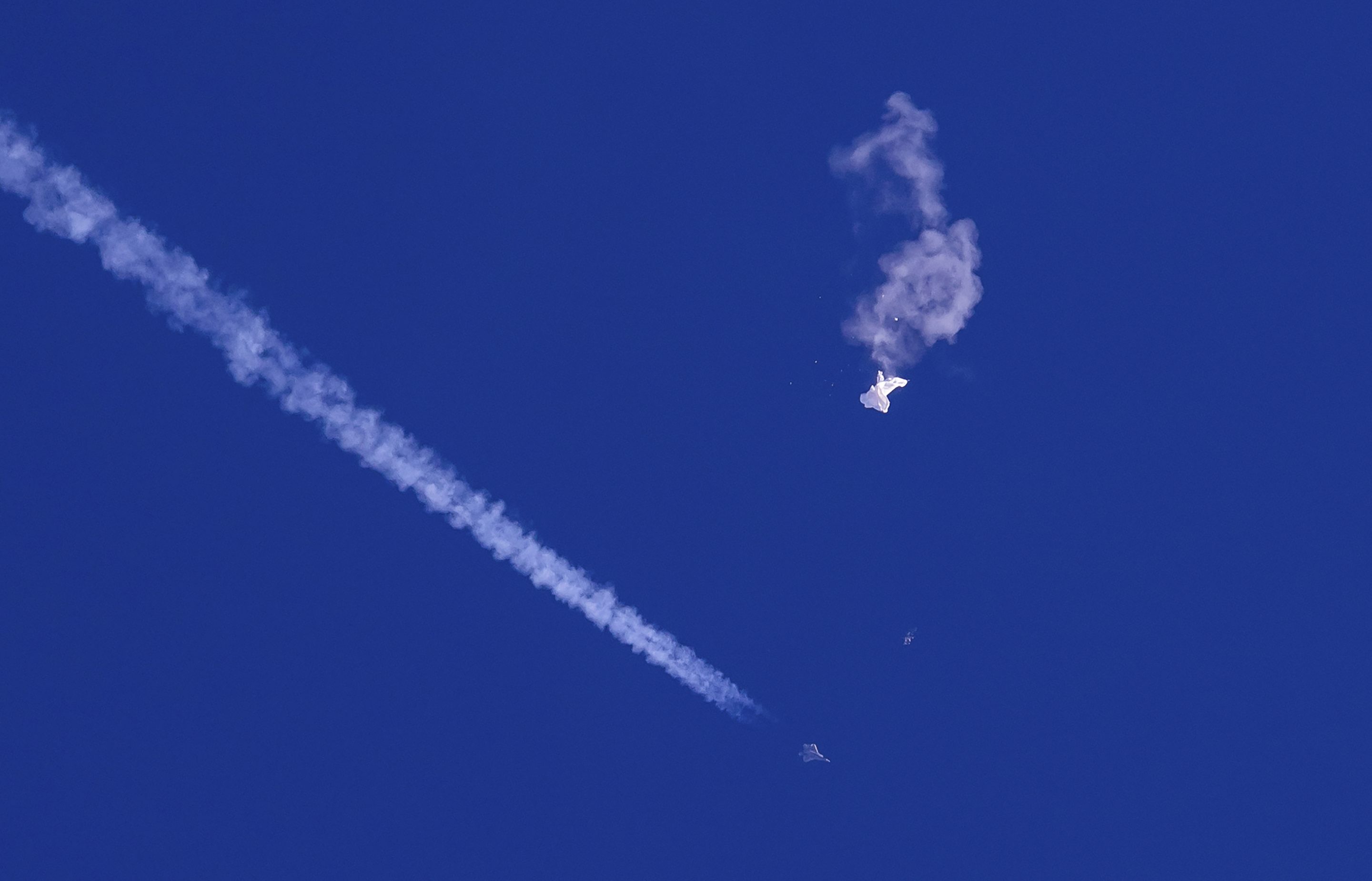 The remnants of a large balloon drift above the Atlantic Ocean, just off the coast of South Carolina, with a fighter jet and its contrail seen below it, on Feb. 4, 2023.