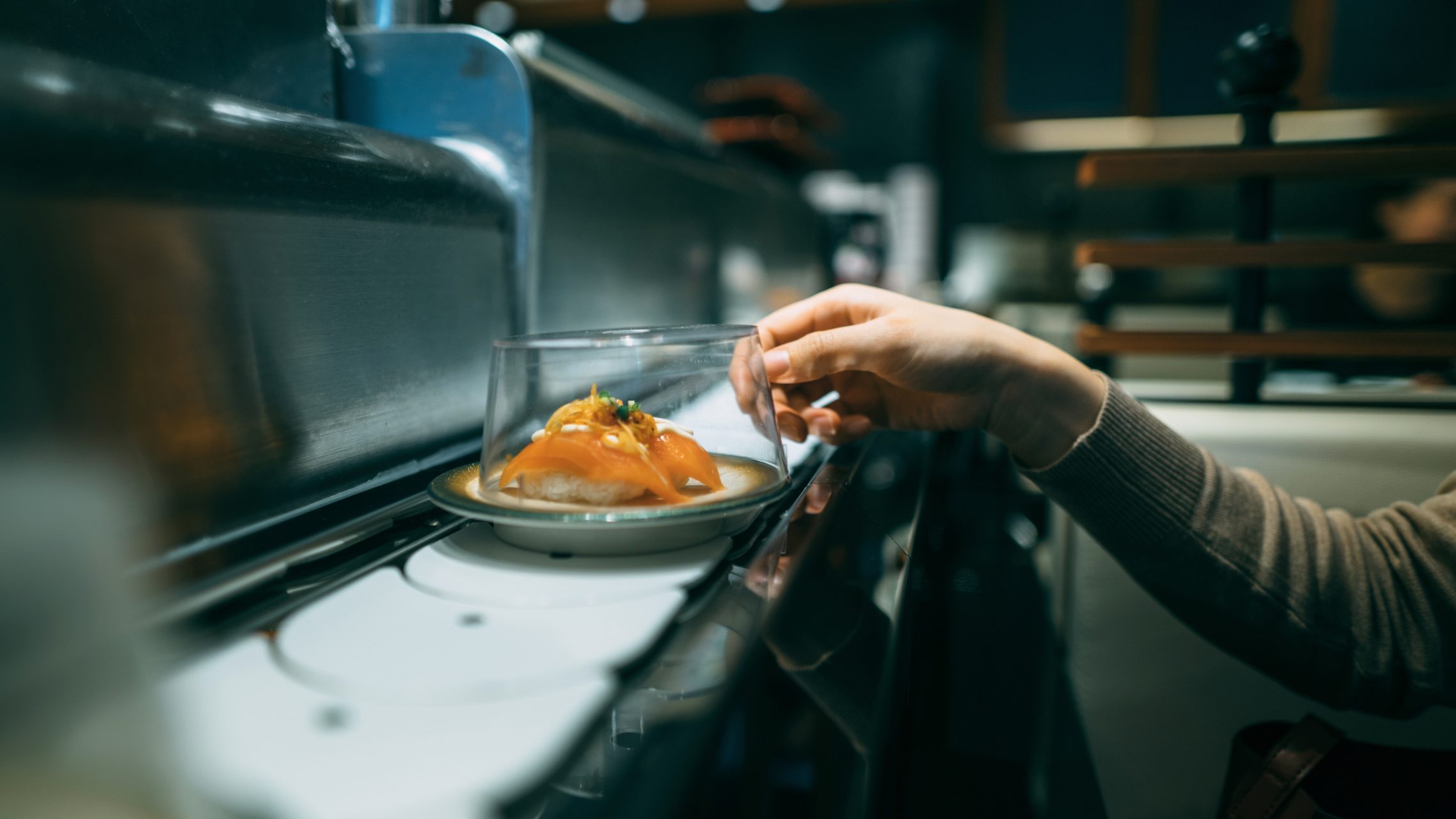 Human's hand picking up sushi dish at sushi bar in the Japanese restaurant