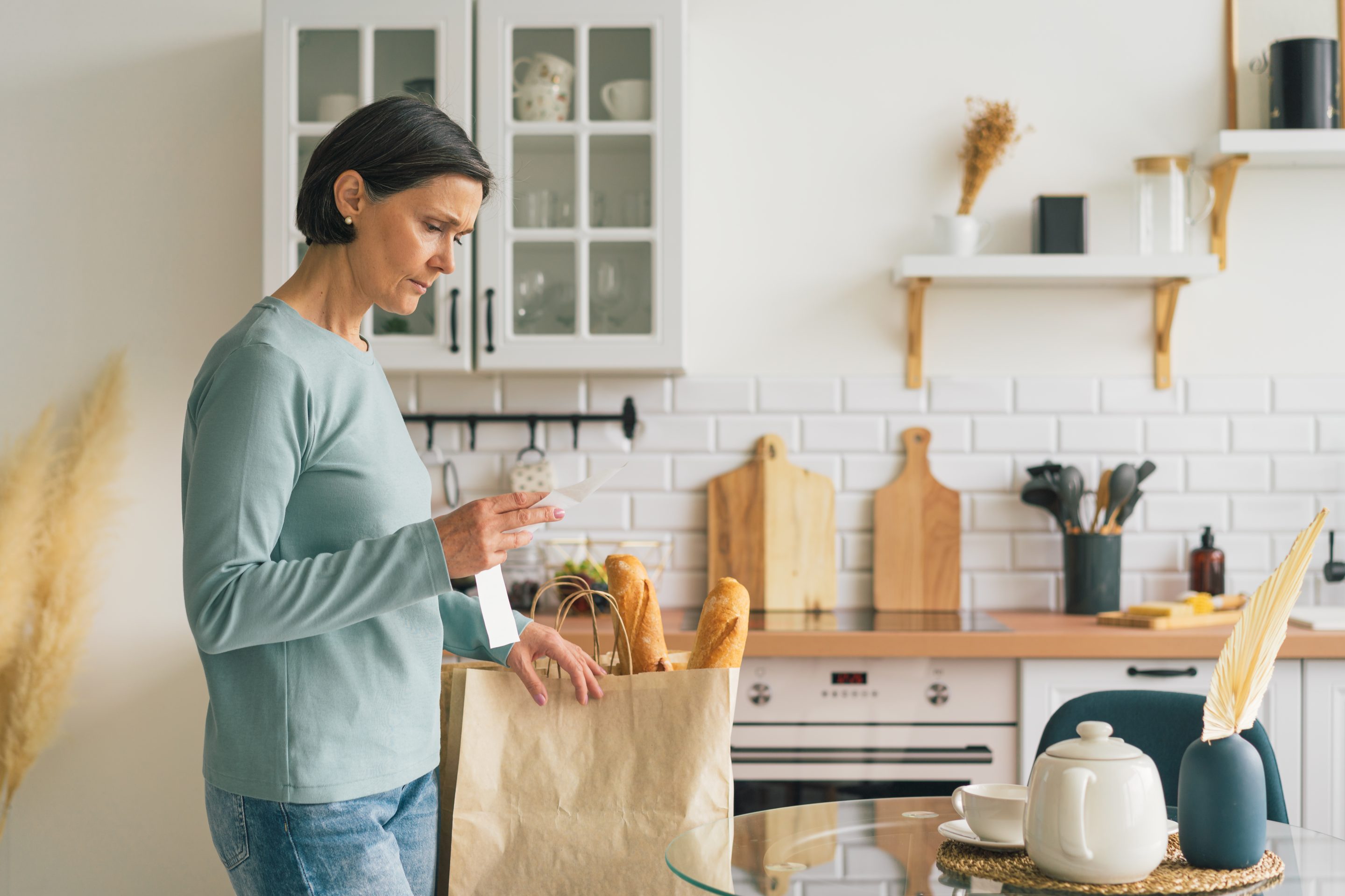 Senior woman frustrated while looking at receipt from grocery store. Rise in price of products concept. Buying consumer goods during inflation. Wisely planning family budget and managing expenses. Facing economic downturn, copy space