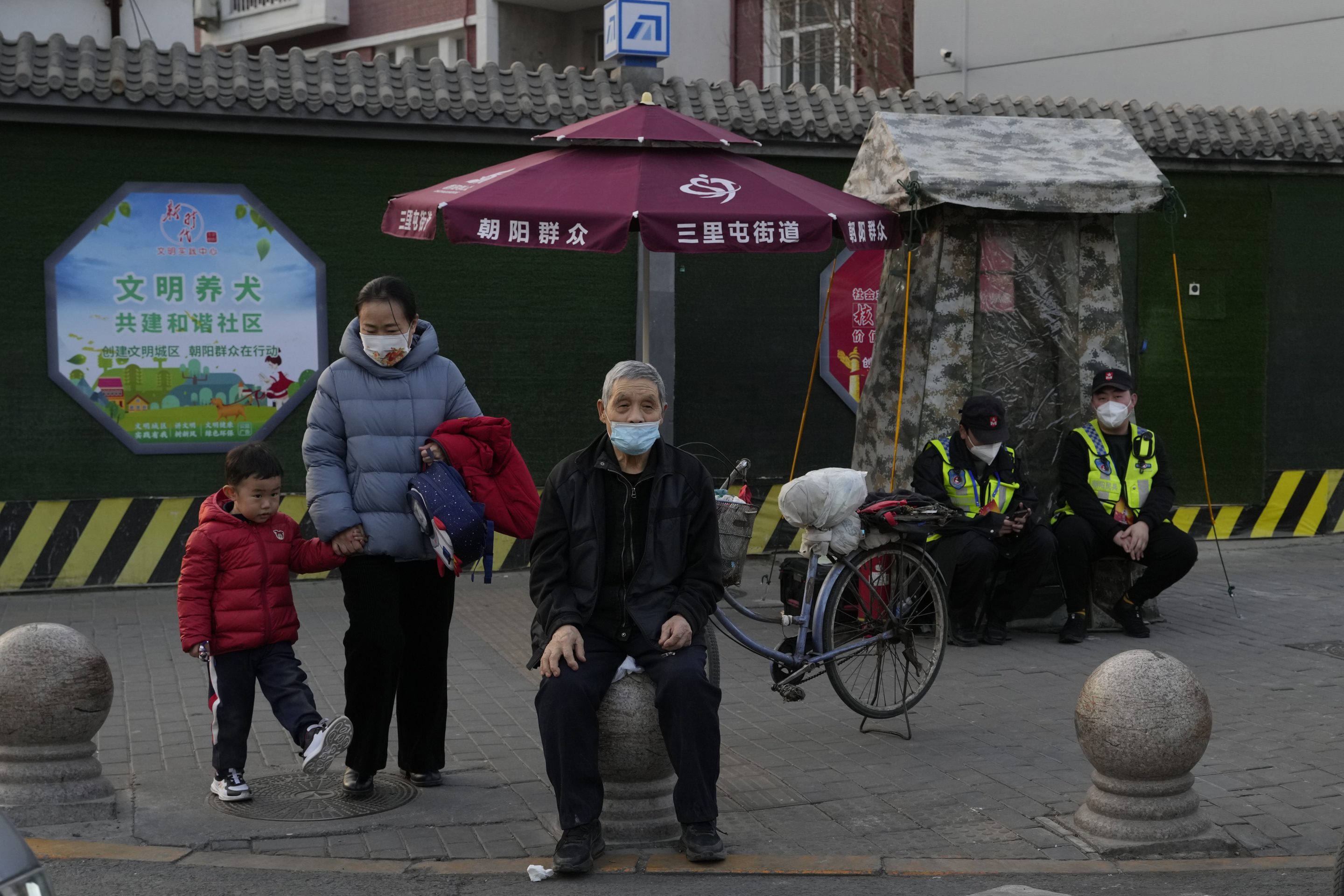 Residents wait to cross a road near members of the Chaoyang militia on duty in Beijing, on March 6, 2023.