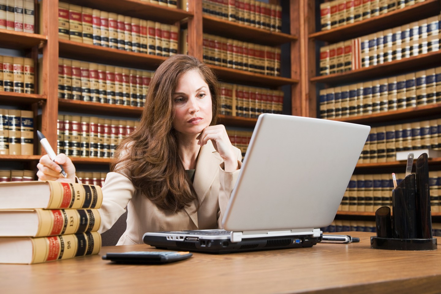 Photo of a woman sitting at a desk looking at a computer in front of a library shelf full of legal books.
