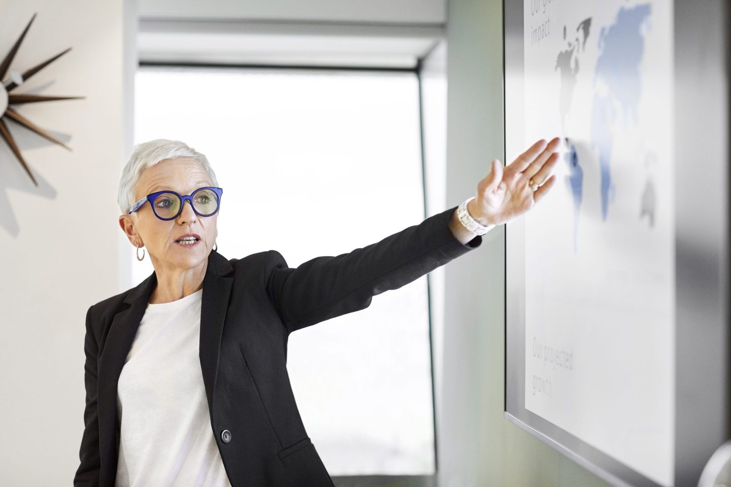 Senior businesswoman gesturing while looking at world map on screen
