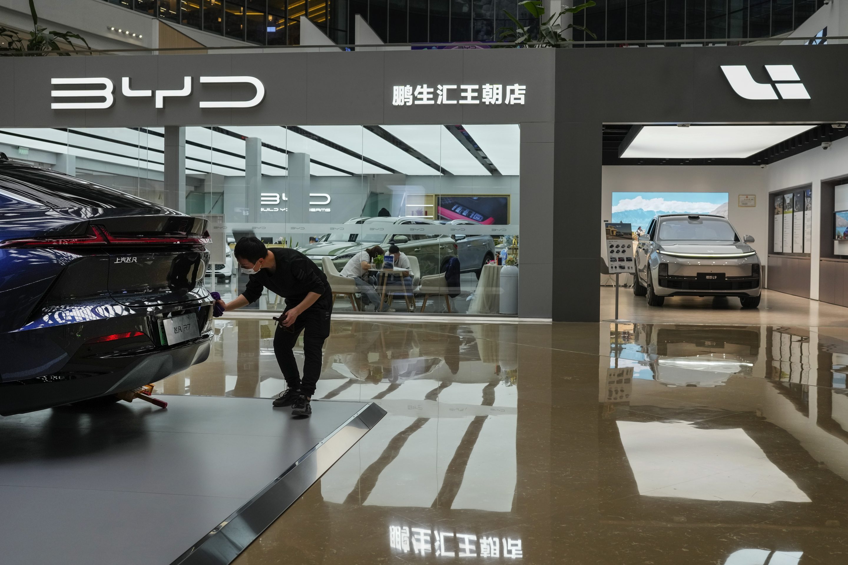 A worker wipes a Rising F7 car model at a floor section selling various Chinese-made electric car brands inside a shopping mall in Beijing, on April 4, 2023.