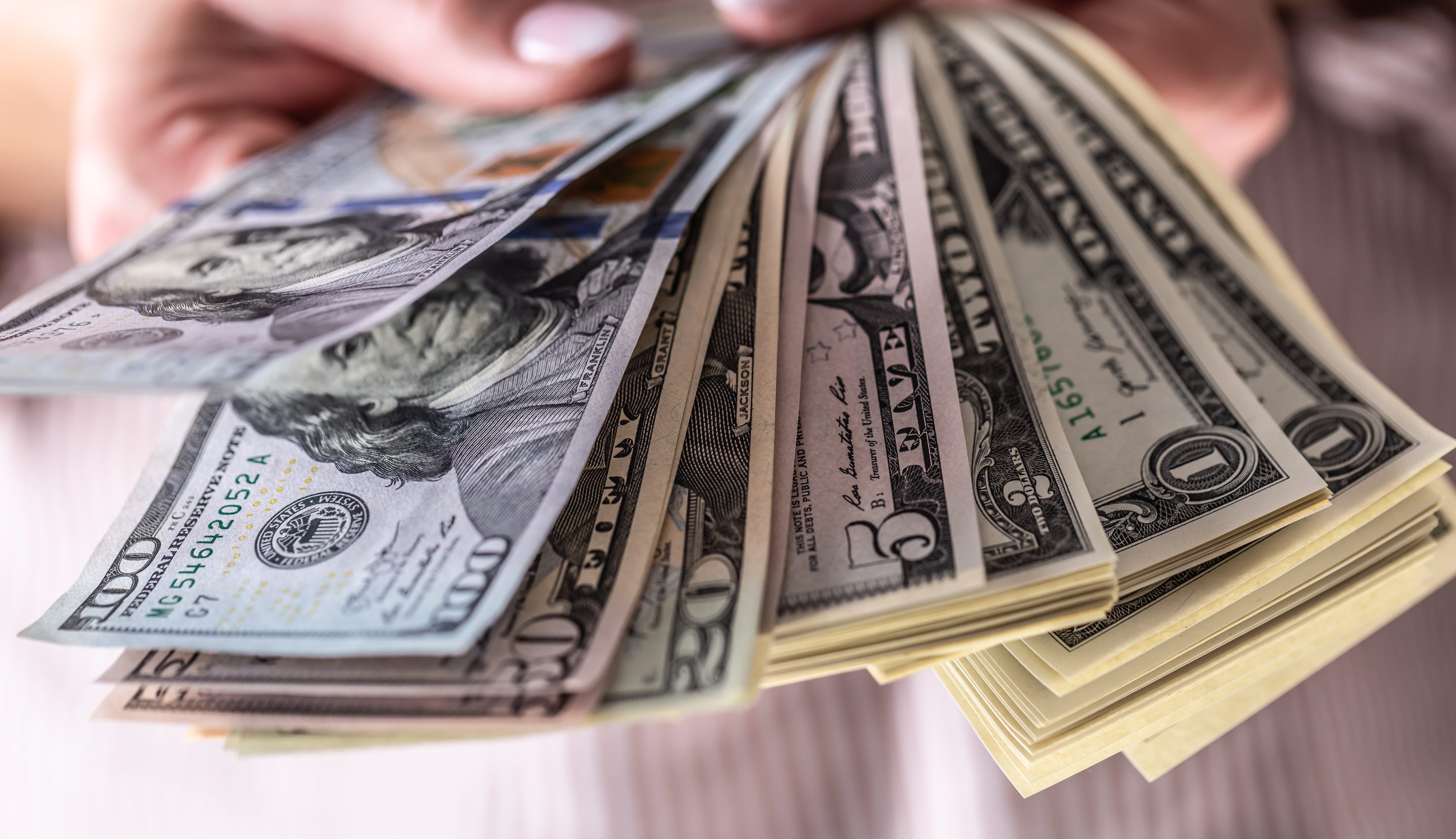 An unseen person holds a fan of U.S. dollar bills.