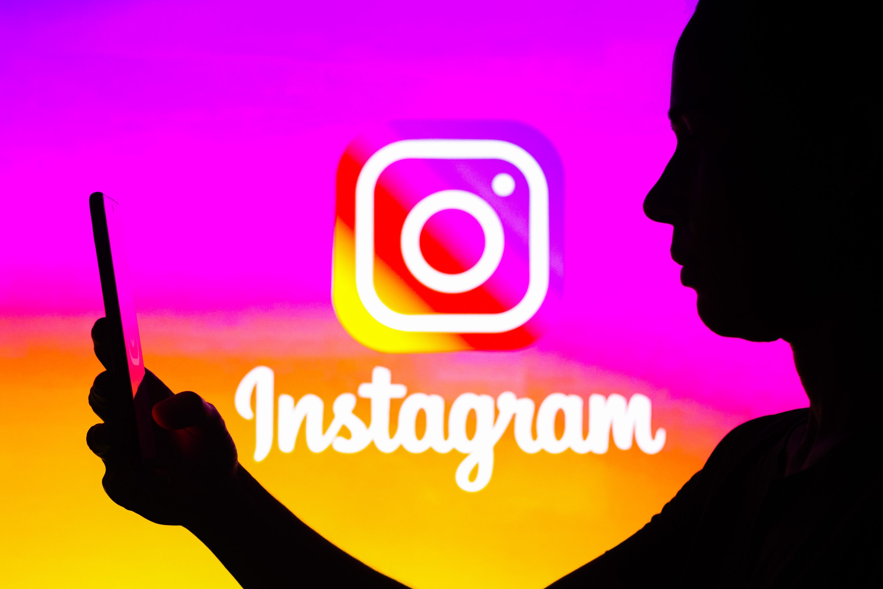 In this photo illustration, a woman's silhouette is holding a smartphone with an Instagram logo in the background.