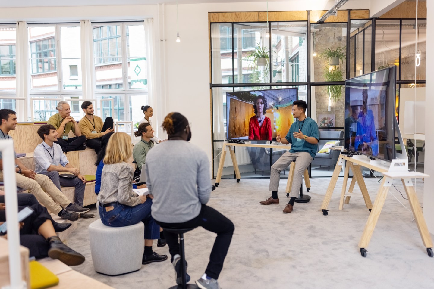 Asian man addressing businesspeople during meeting with two colleagues attending via video call seen on television screen. Business people having hybrid meeting in office.