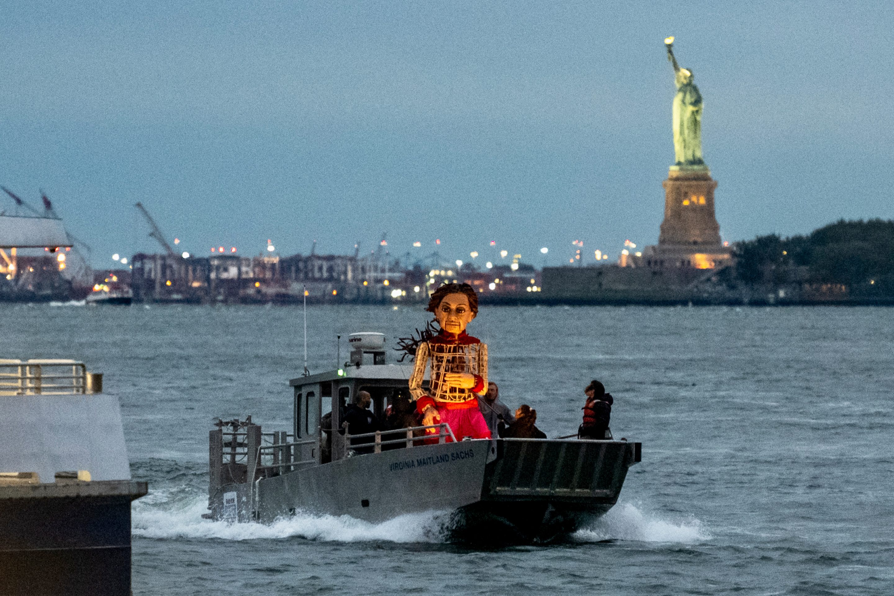 The 12-foot puppet known as "Little Amal" sails past the Statue of Liberty in 2022. The performance art initiative has been touring around the world to raise awareness about the plight of displaced people.