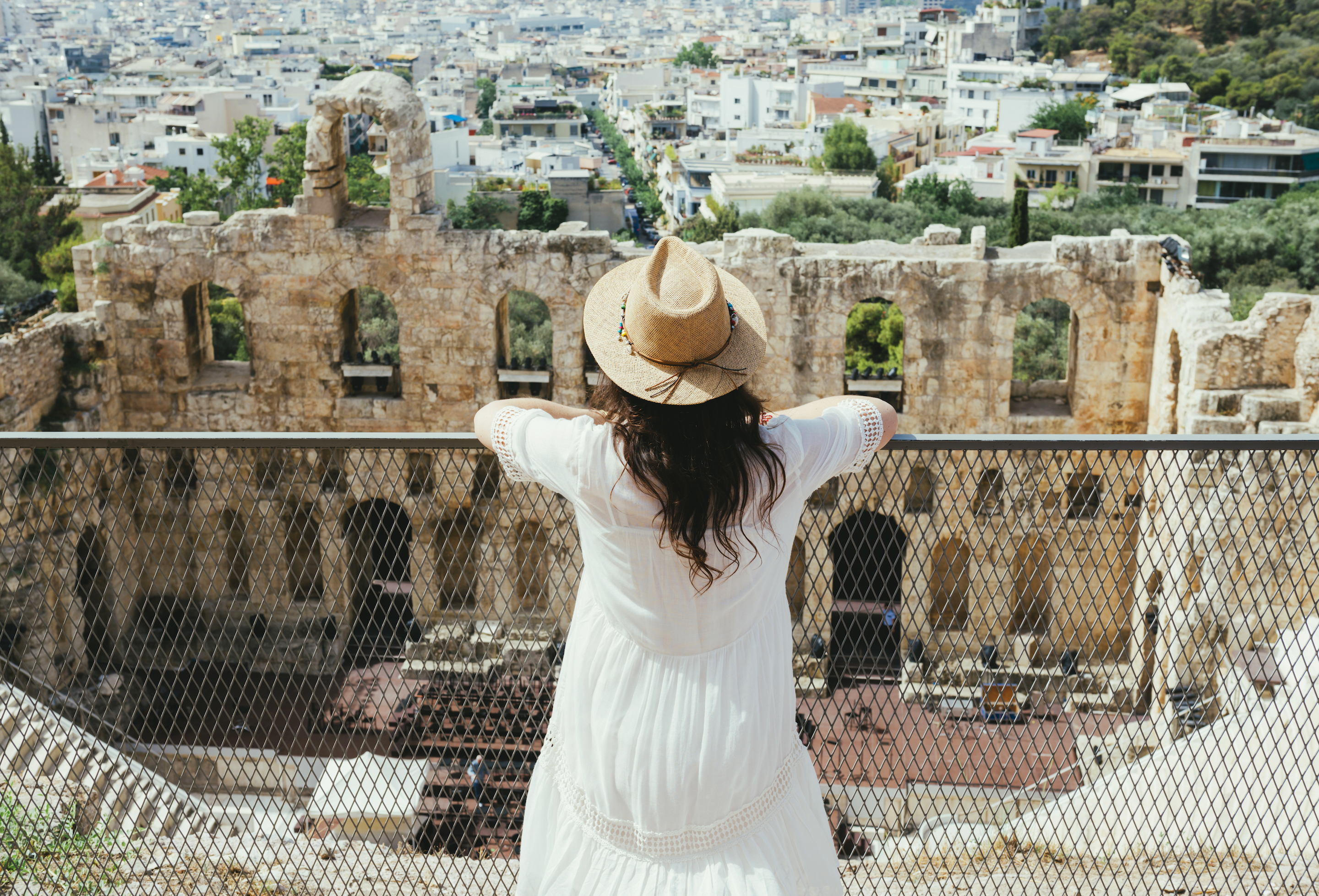 A tourist stands in front of a gate, overlooking the Temple of Dionysus at the Acropolis of Athens.