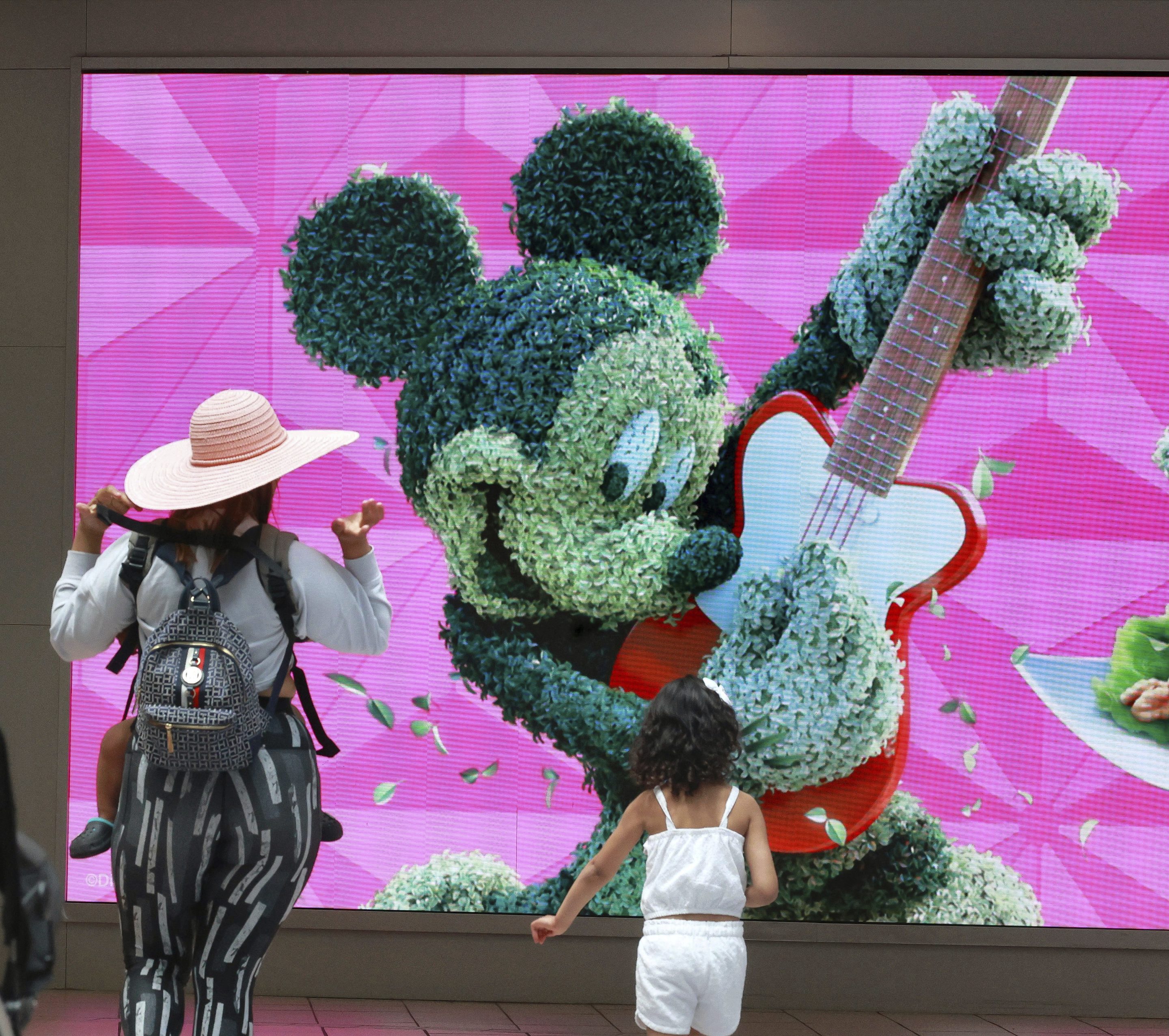 Travelers check out a jumbo screen projecting images of Walt Disney World in the east hall atrium at Orlando International Airport, Thursday, May 25, 2023 in Orlando, Fla.