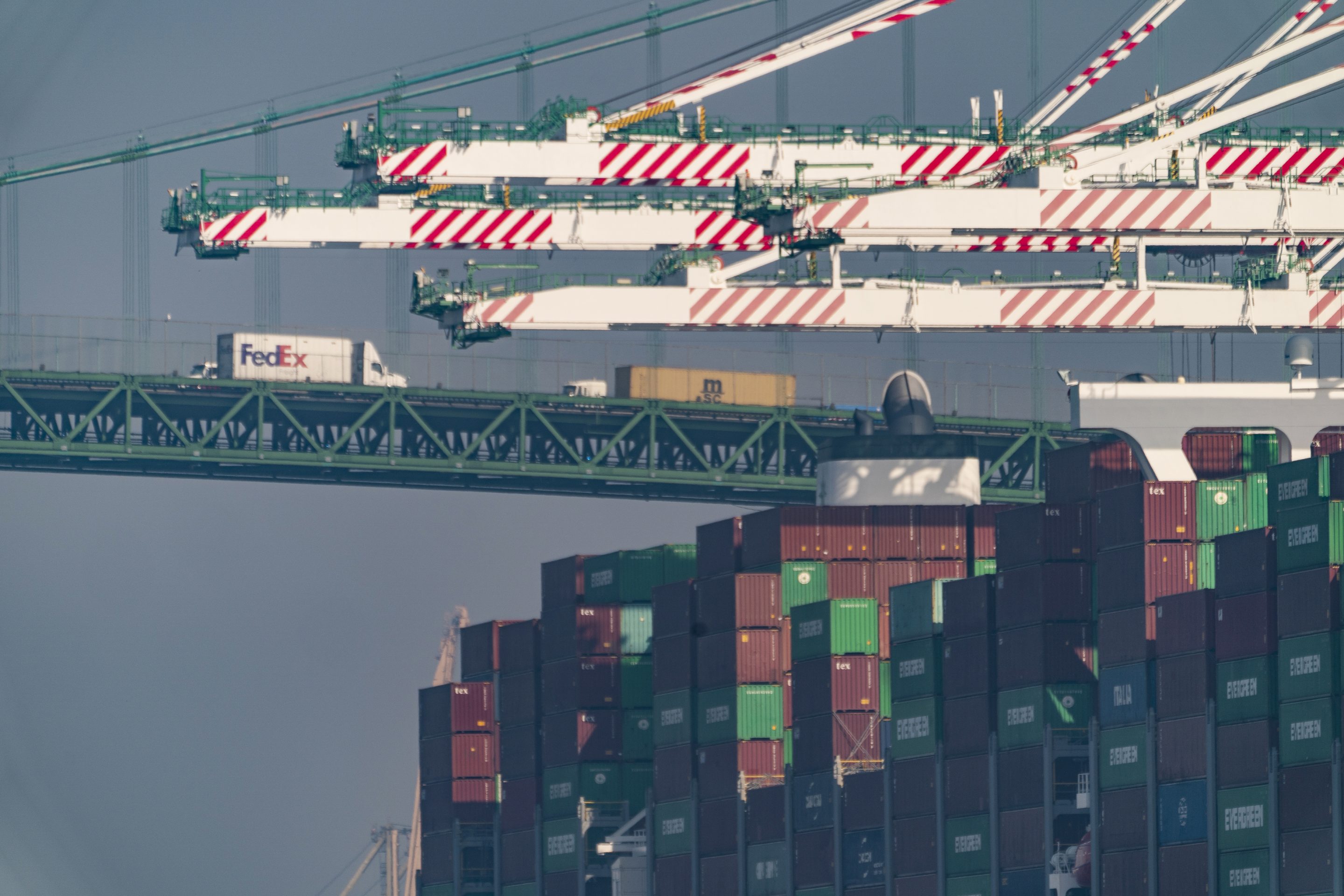 Transportation trucks cross the Vincent Thomas Bridge over the main channel as shipping containers are seen stacked on the Evergreen terminal at the Port of Los Angeles in San Pedro, Calif., Nov. 30, 2021.