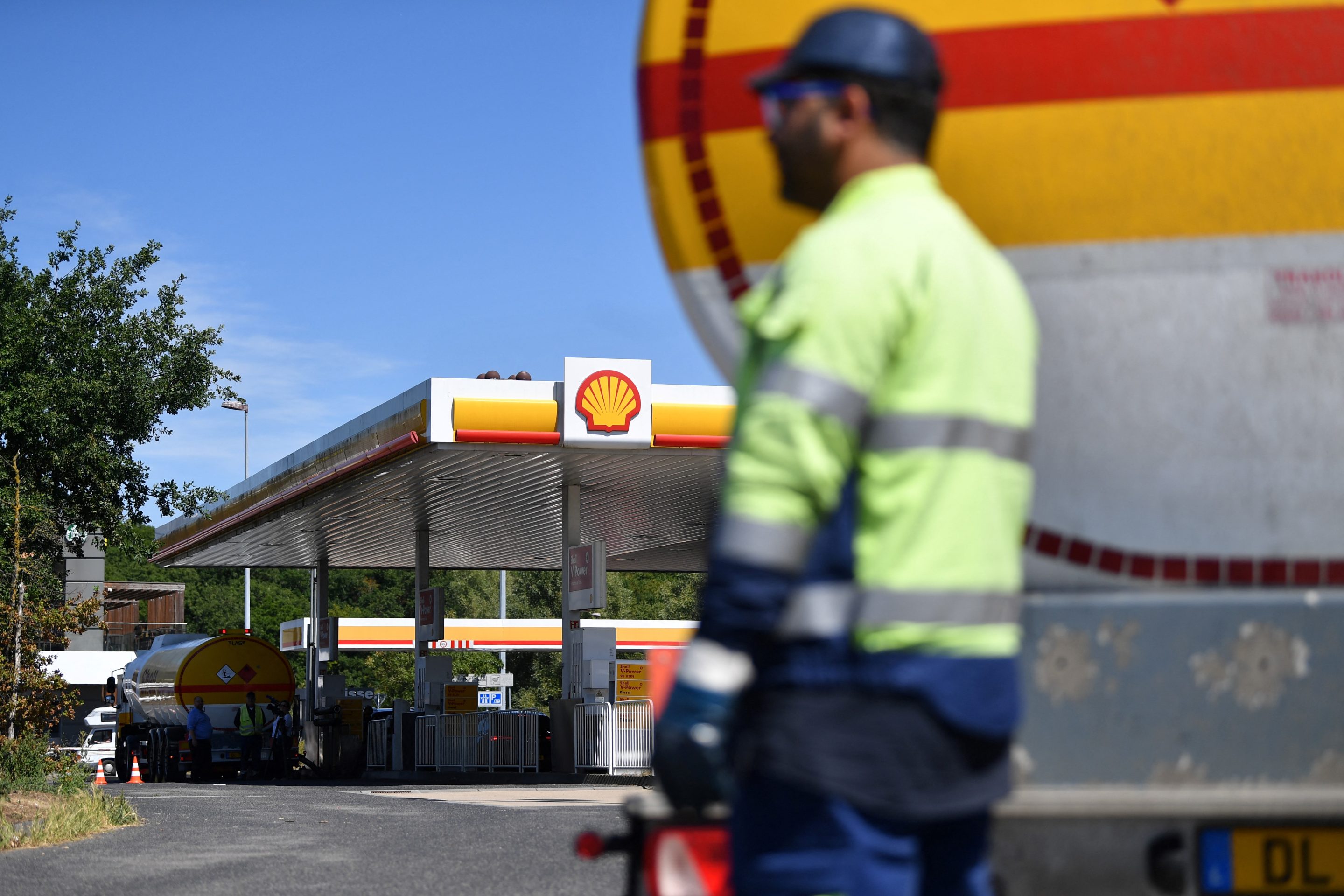 A truck driver stands by the gas container of his truck at a Shell gas station