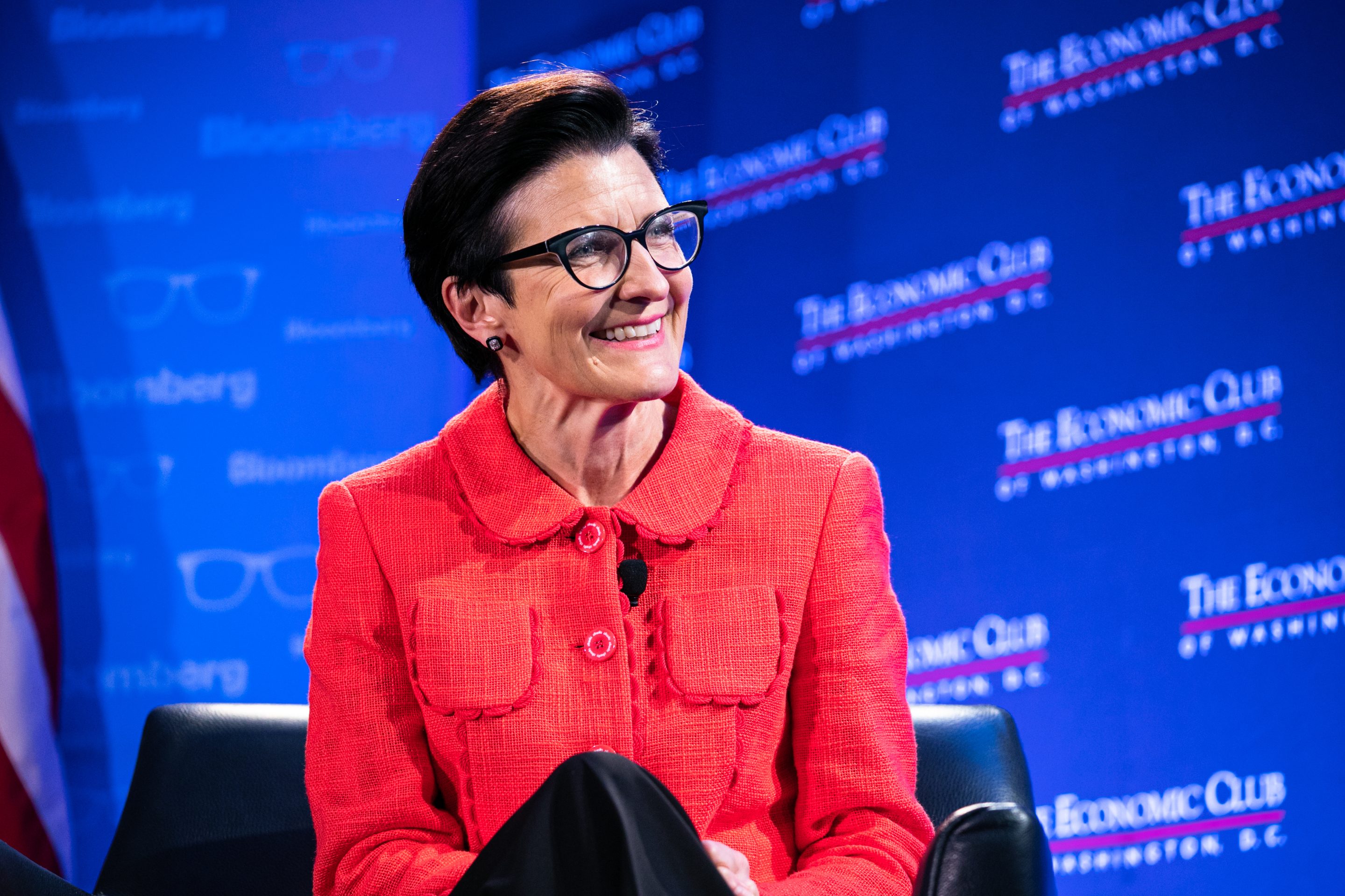 Woman wearing glasses and red jacket sitting on stage