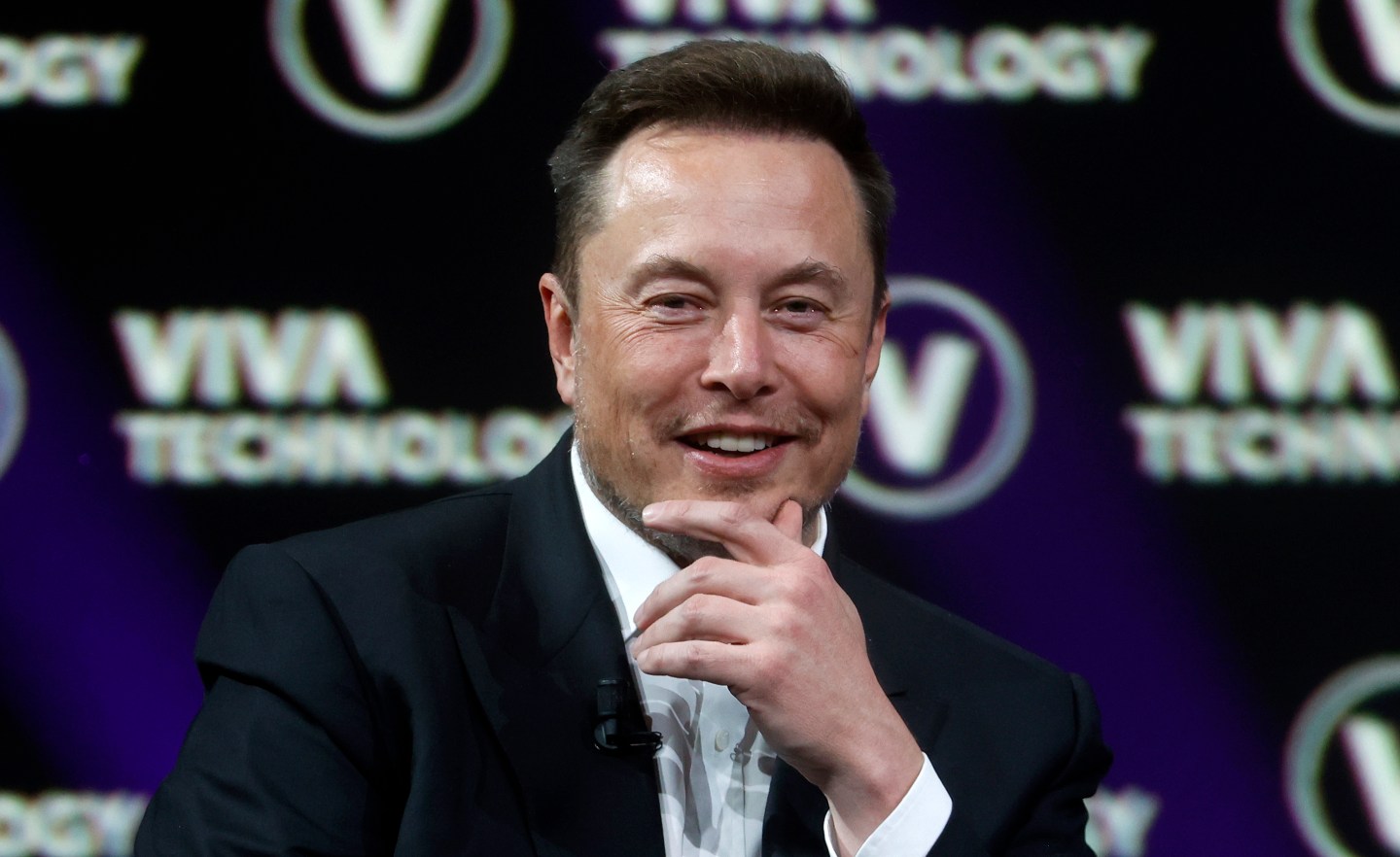 A picture of Elon Musk holding his hand to his chin and smiling slightly