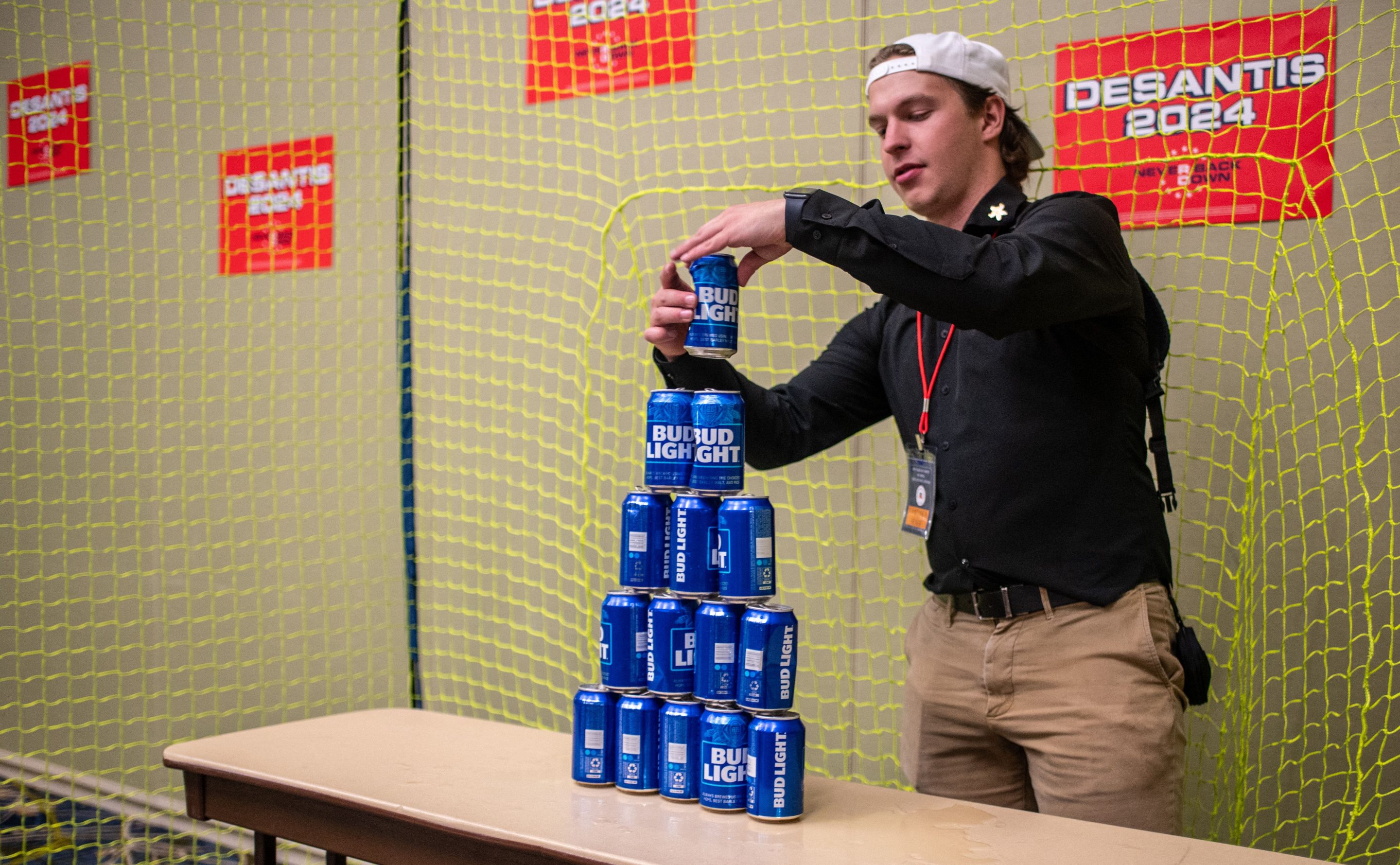 An employee builds a tower of Bud Light beer cans for "ball target practice" in the Ron DeSantis booth at the Republican Party of Iowa's 2023 Lincoln Dinner on Jul. 28.