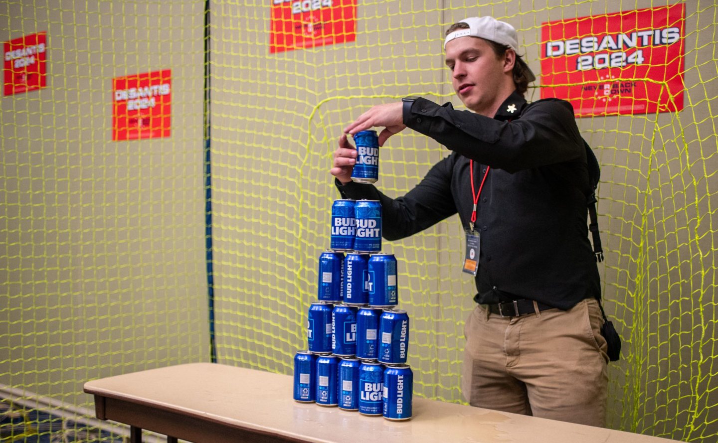 An employee builds a tower of Bud Light beer cans for "ball target practice" in the Ron DeSantis booth at the Republican Party of Iowa's 2023 Lincoln Dinner on Jul. 28.
