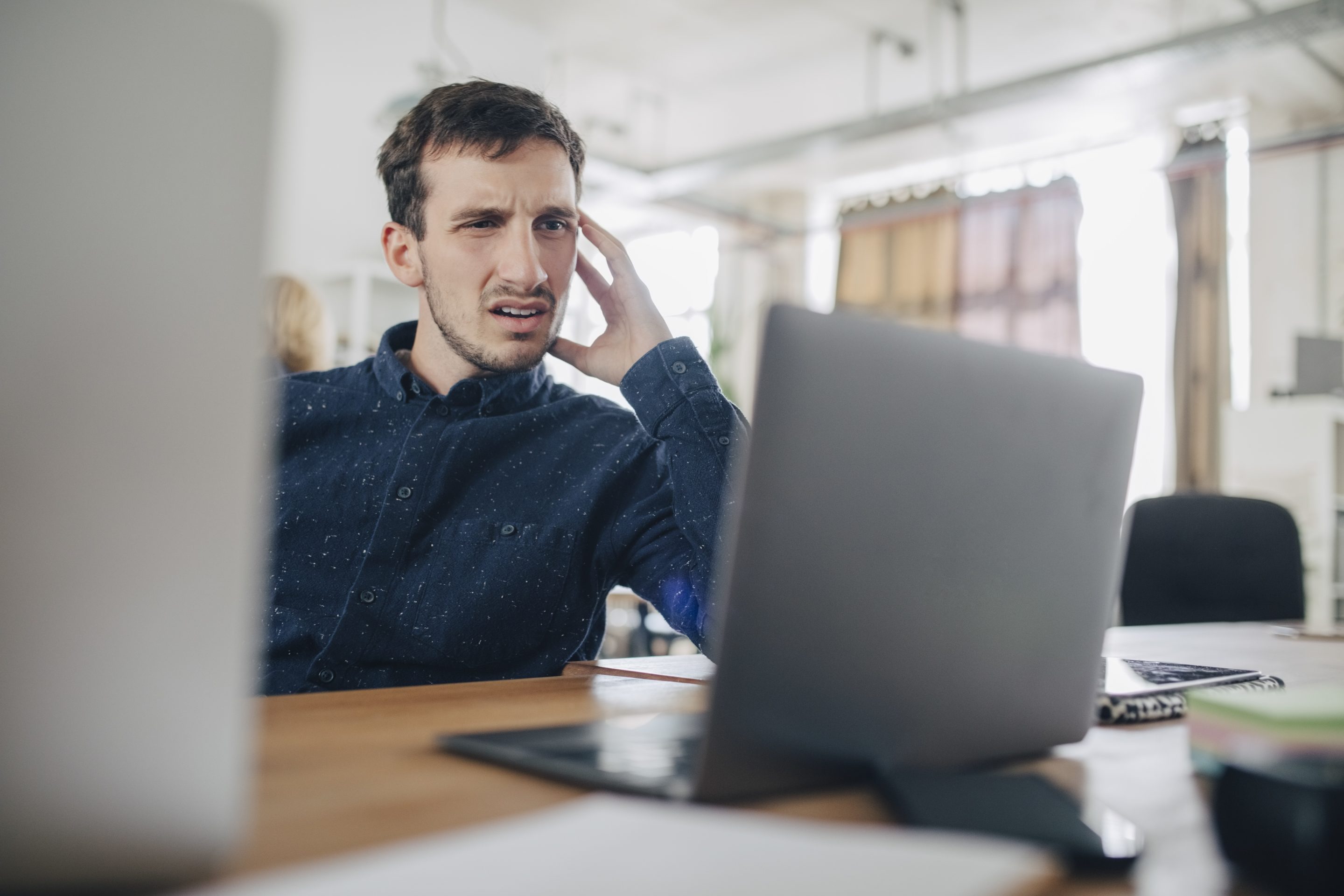 Confused businessman looking at laptop while sitting at desk in office