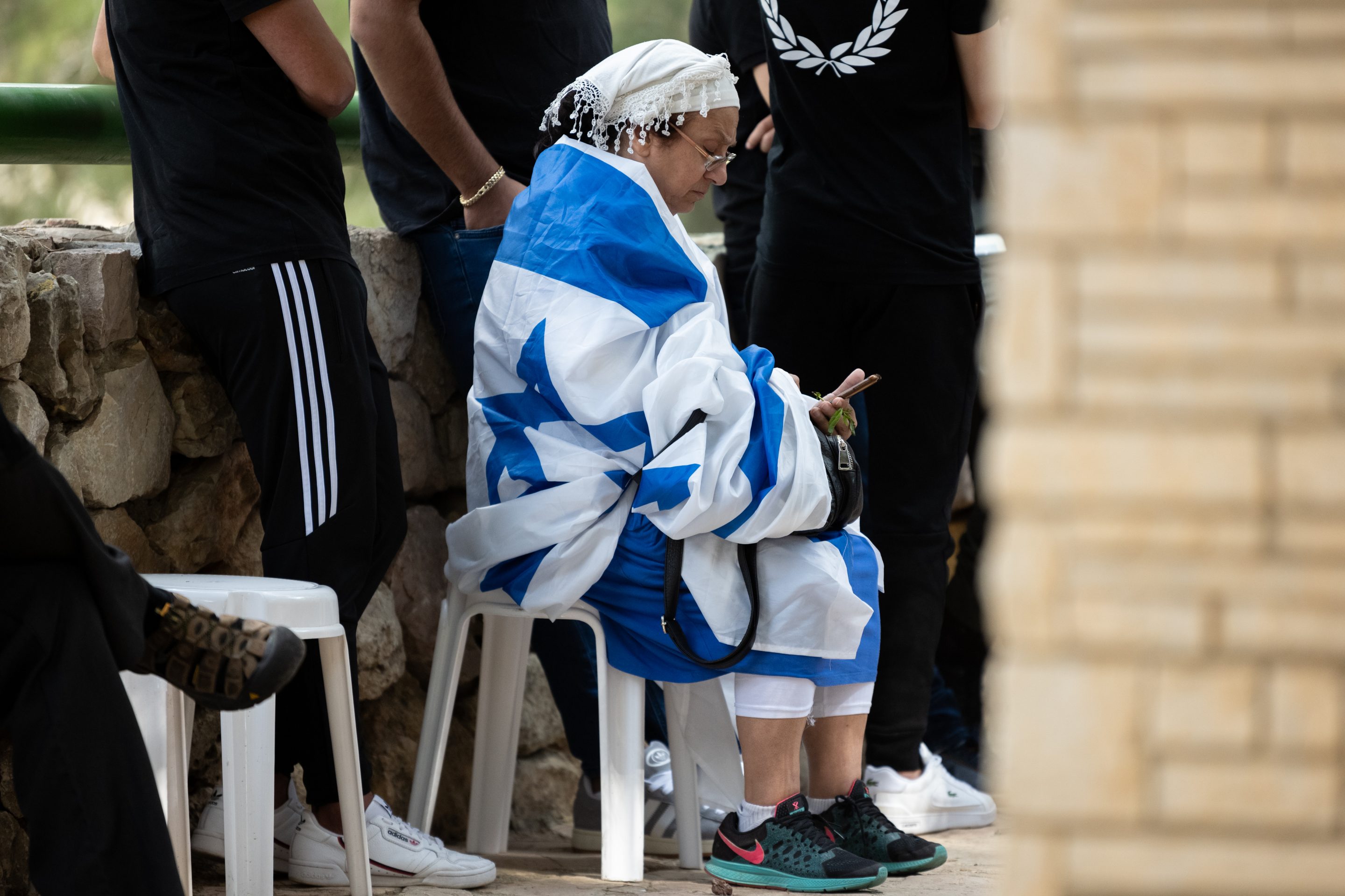 A woman sits draped in an Israeli flag next to a grave during a funeral ceremony on Oct. 12, 2023, at Mount Herzl Military Cemetery in Jerusalem.